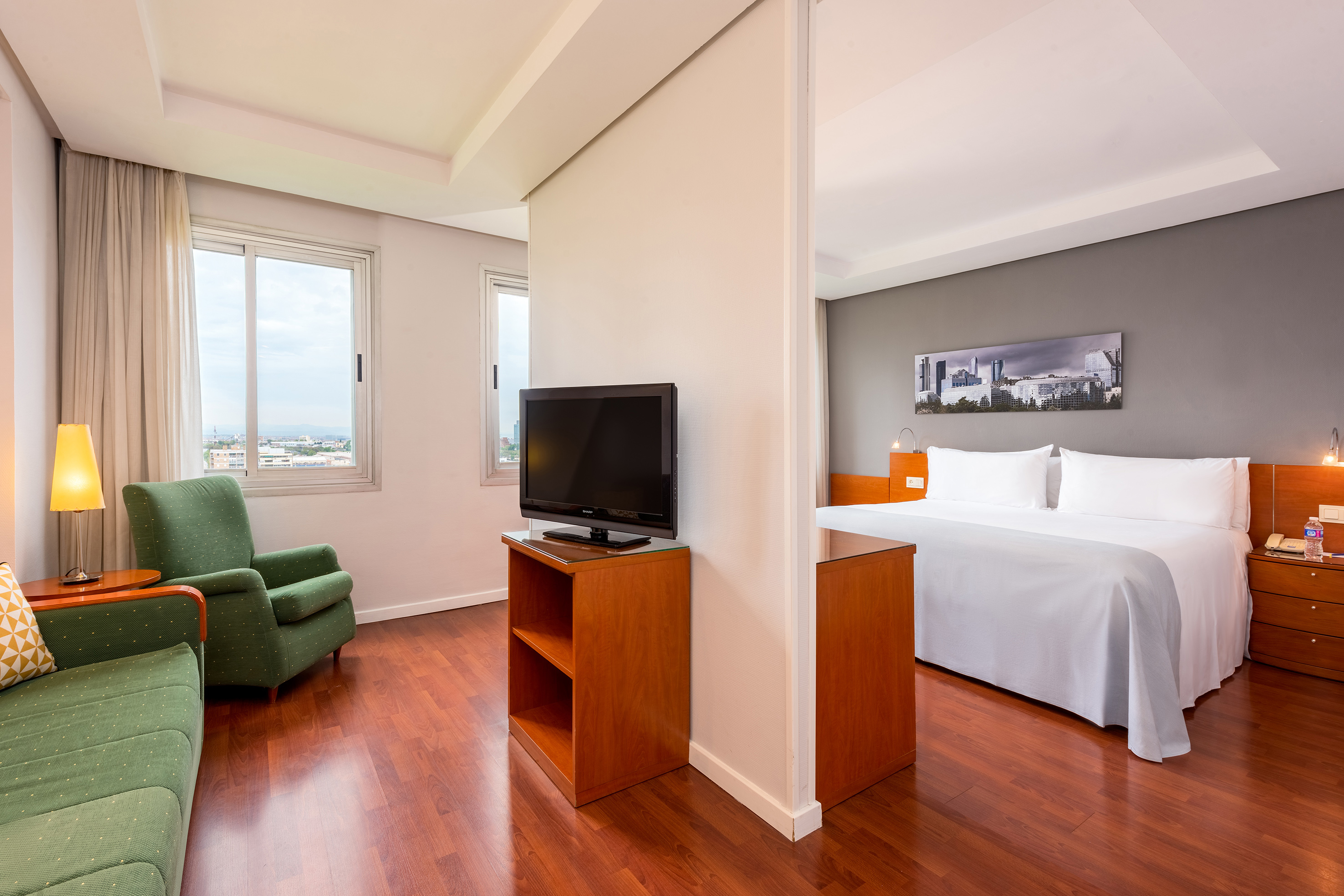 Hotel suite with living room, sofa, TV, king bedroom, and city view.