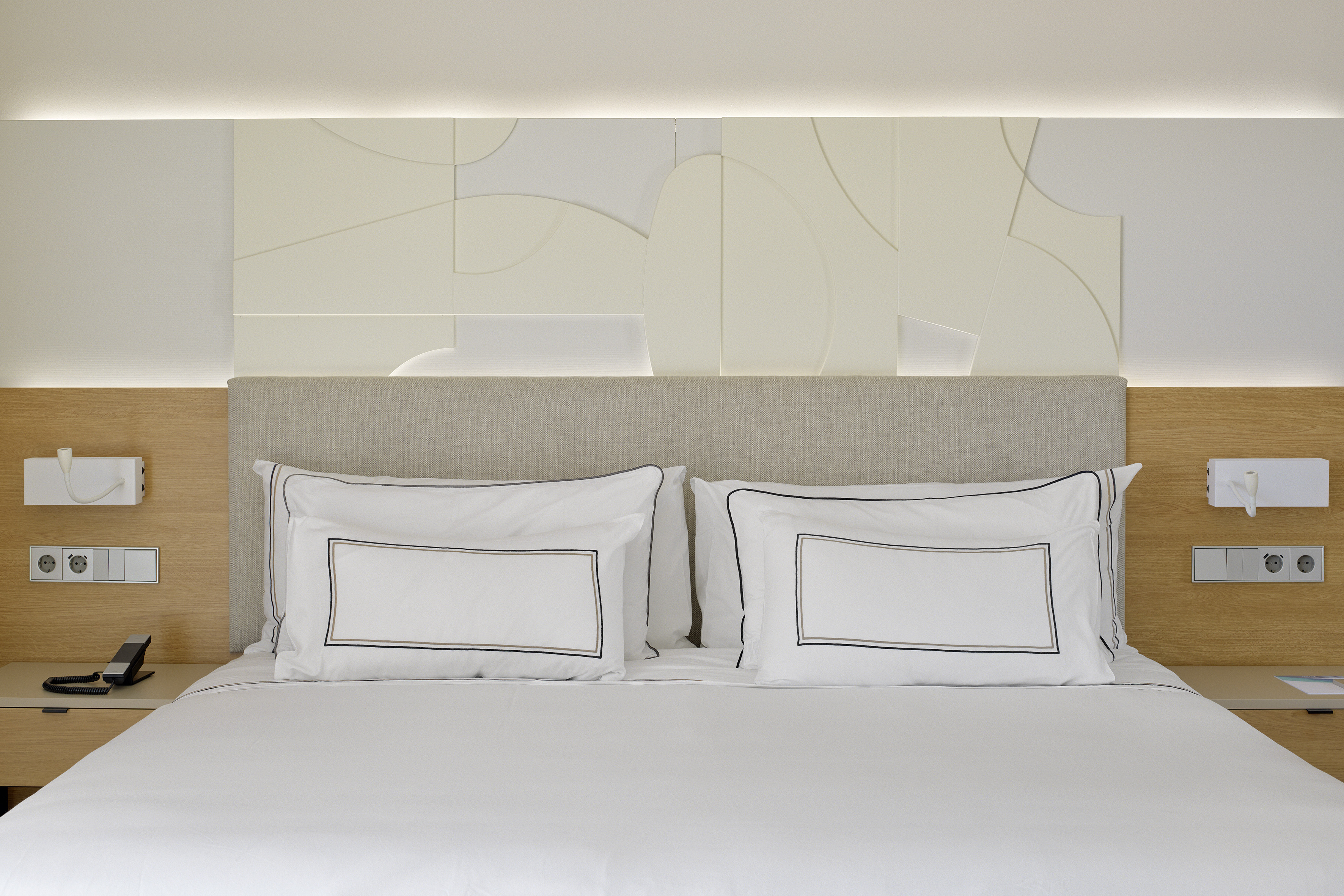 Modern hotel bed, white linens, upholstered headboard, abstract wall decor.