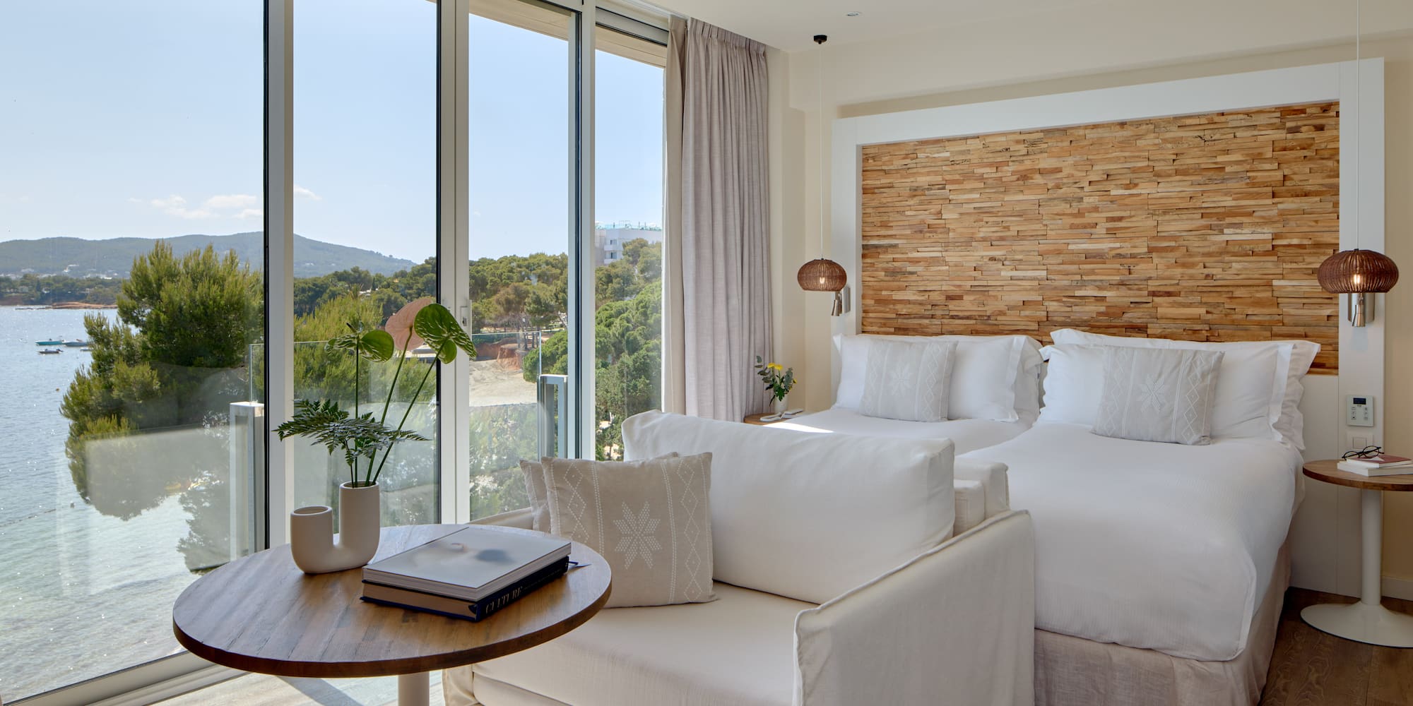 Modern coastal hotel room with sea view, two beds, and stylish wooden features.