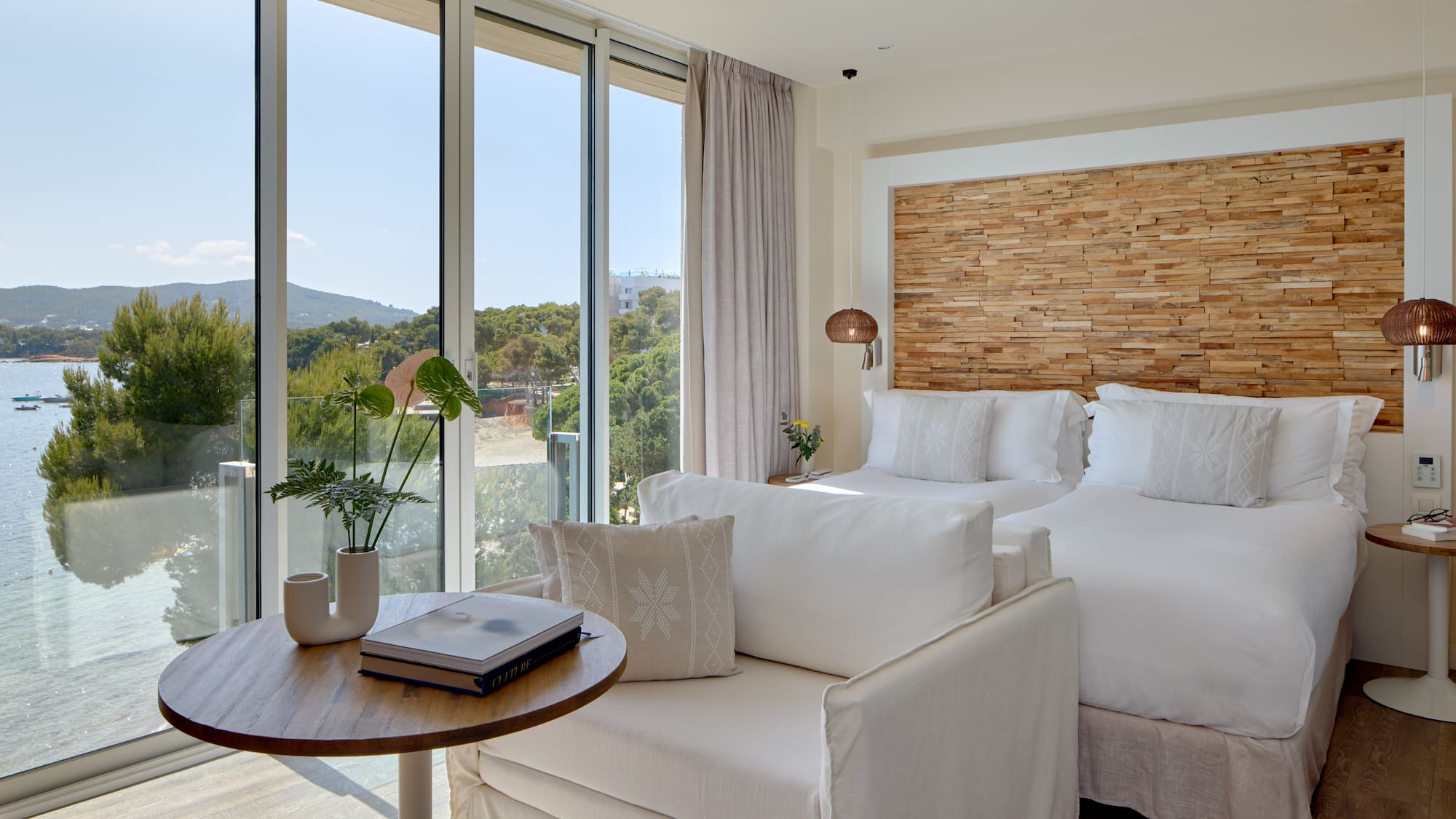Modern coastal hotel room with sea view, two beds, and stylish wooden features.
