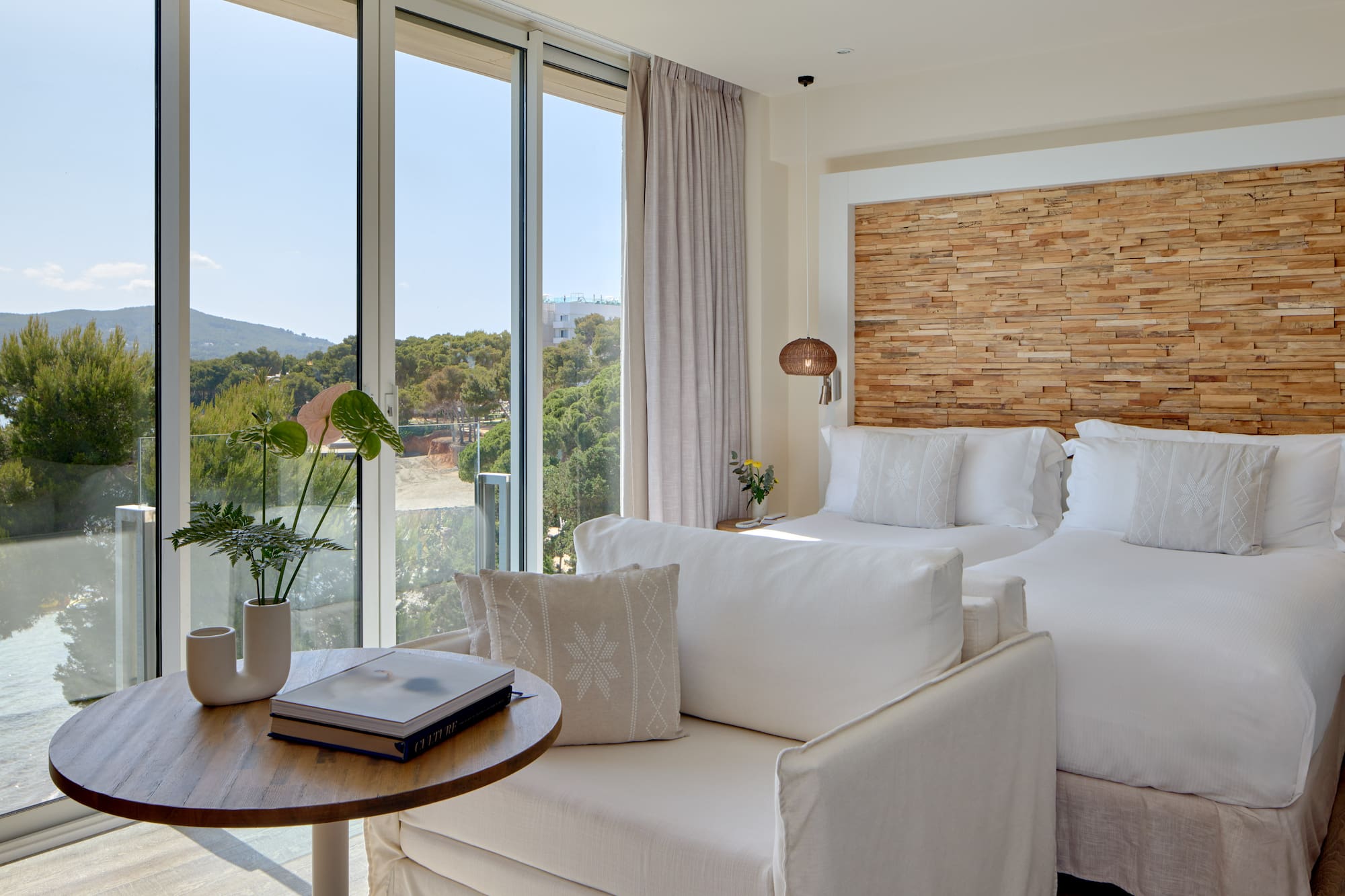 Modern coastal hotel room with sea view, two beds, and stylish wooden features.