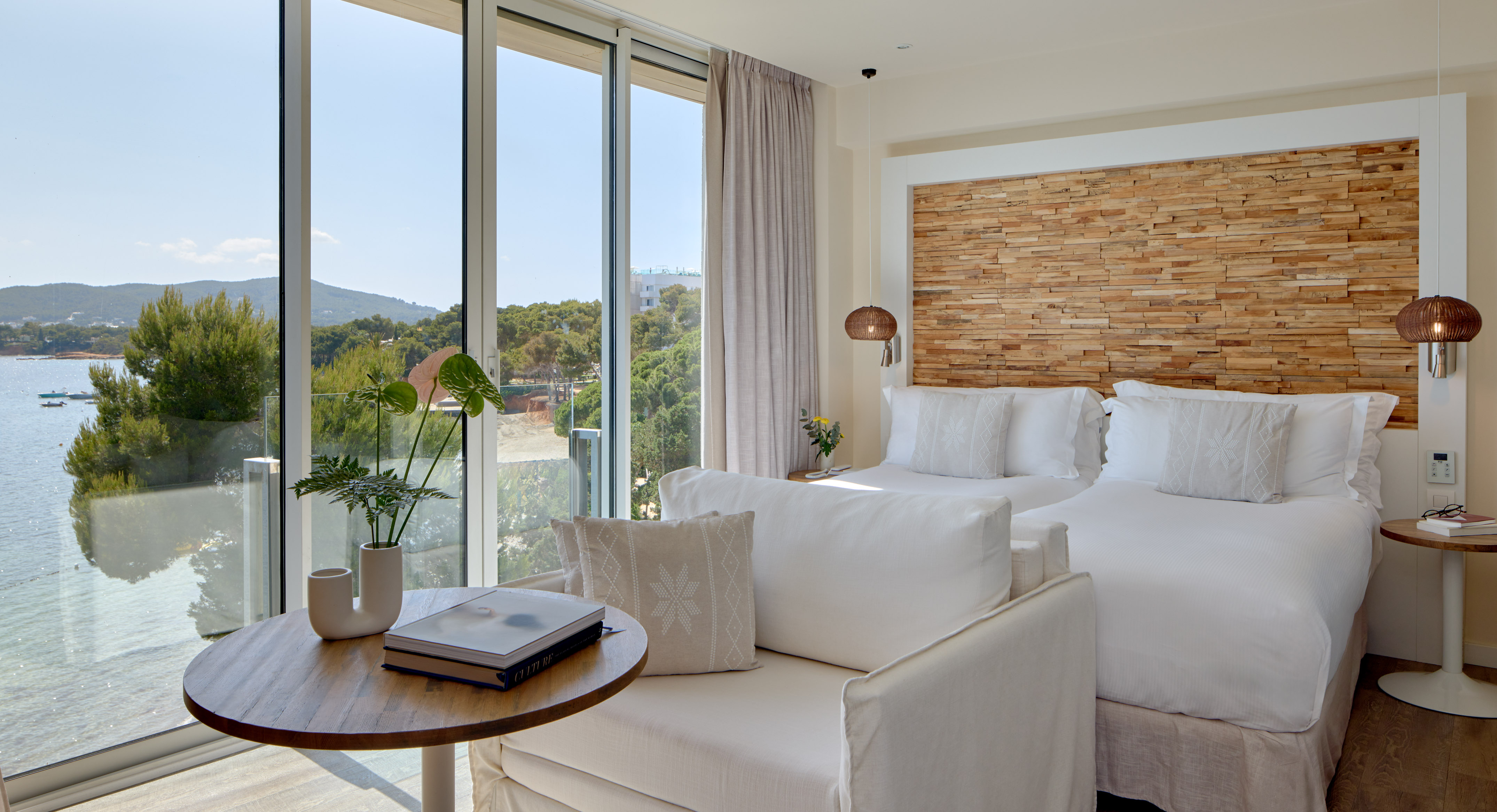 Modern coastal hotel room with sea view, two beds, and stylish wooden features.