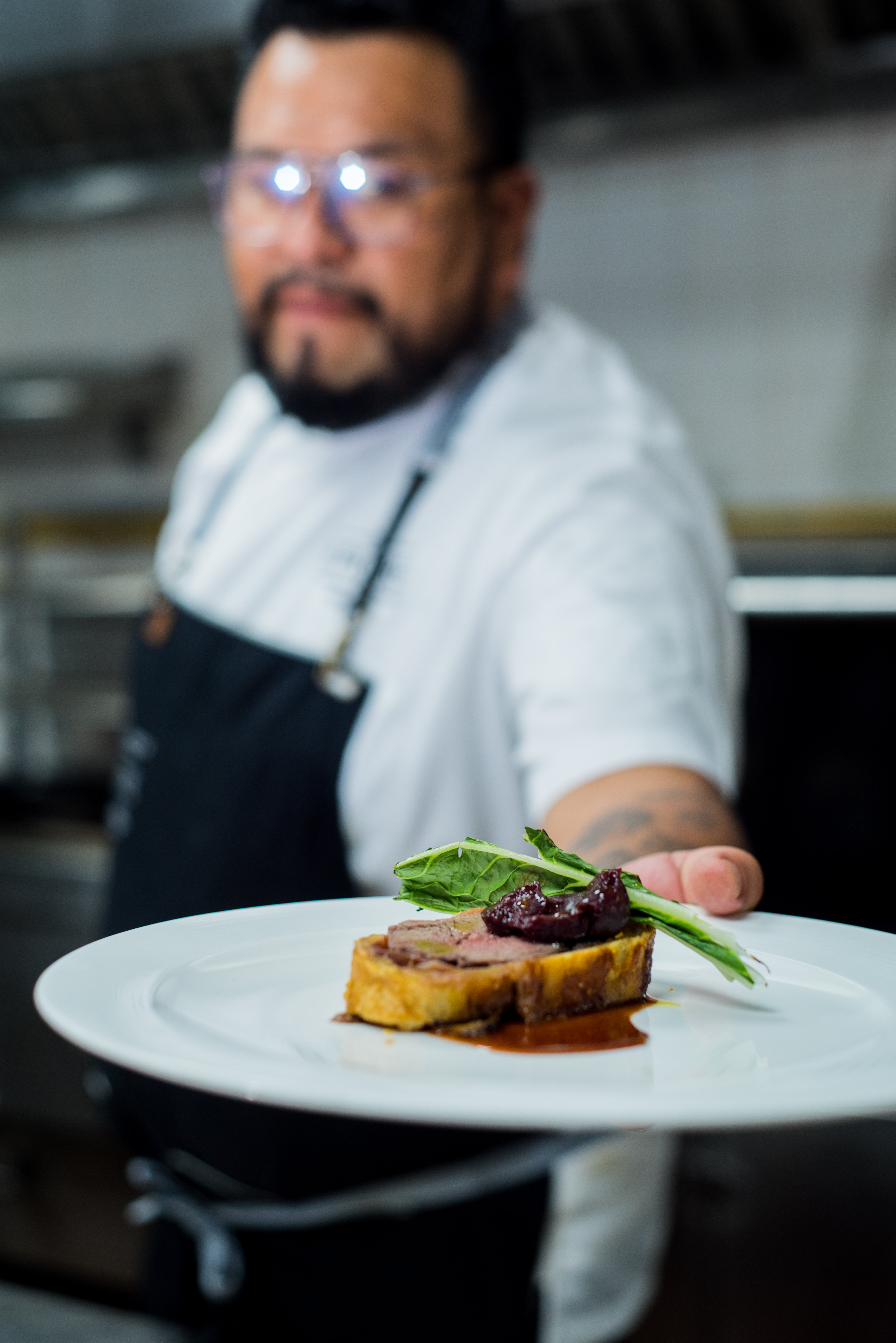 Chef presenting a gourmet beef Wellington dish with berry compote and greens.