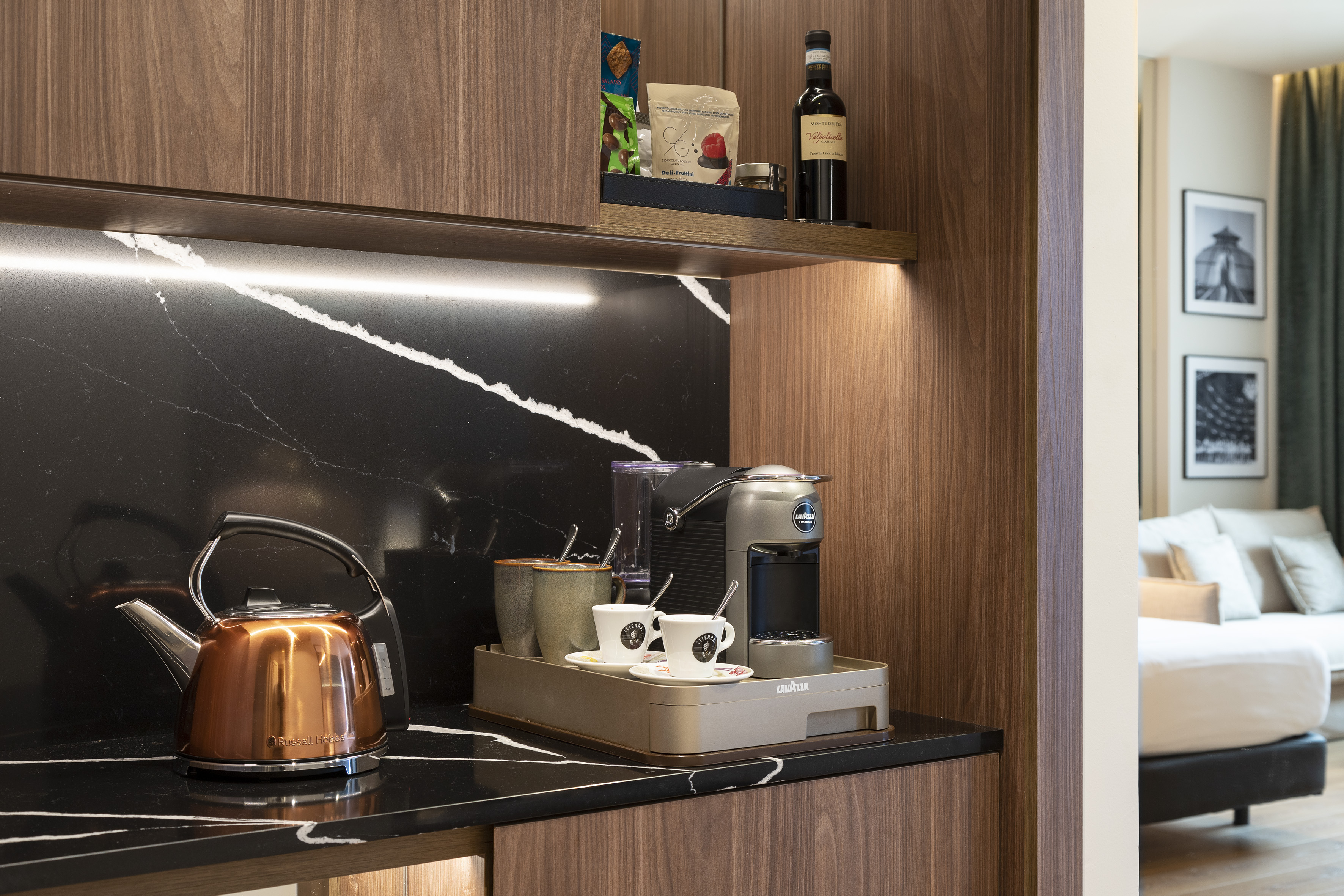 Modern hotel room minibar with Lavazza coffee machine and copper kettle.
