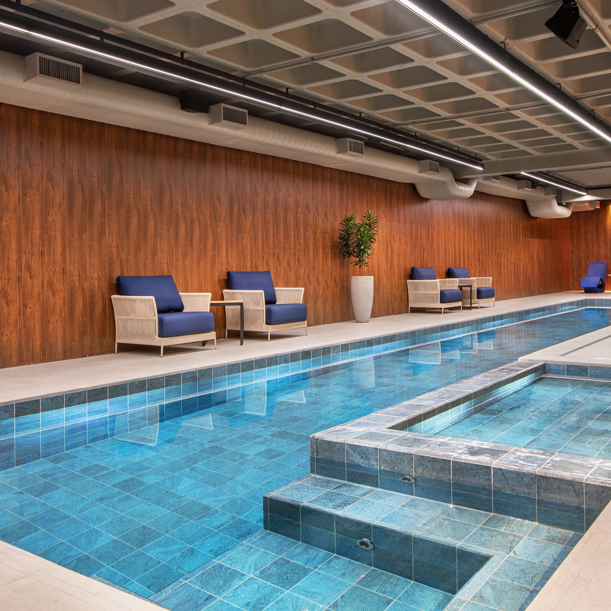 Modern indoor pool with blue tiles, lounge chairs, and wood paneling. - Meliá Paulista, São Paulo