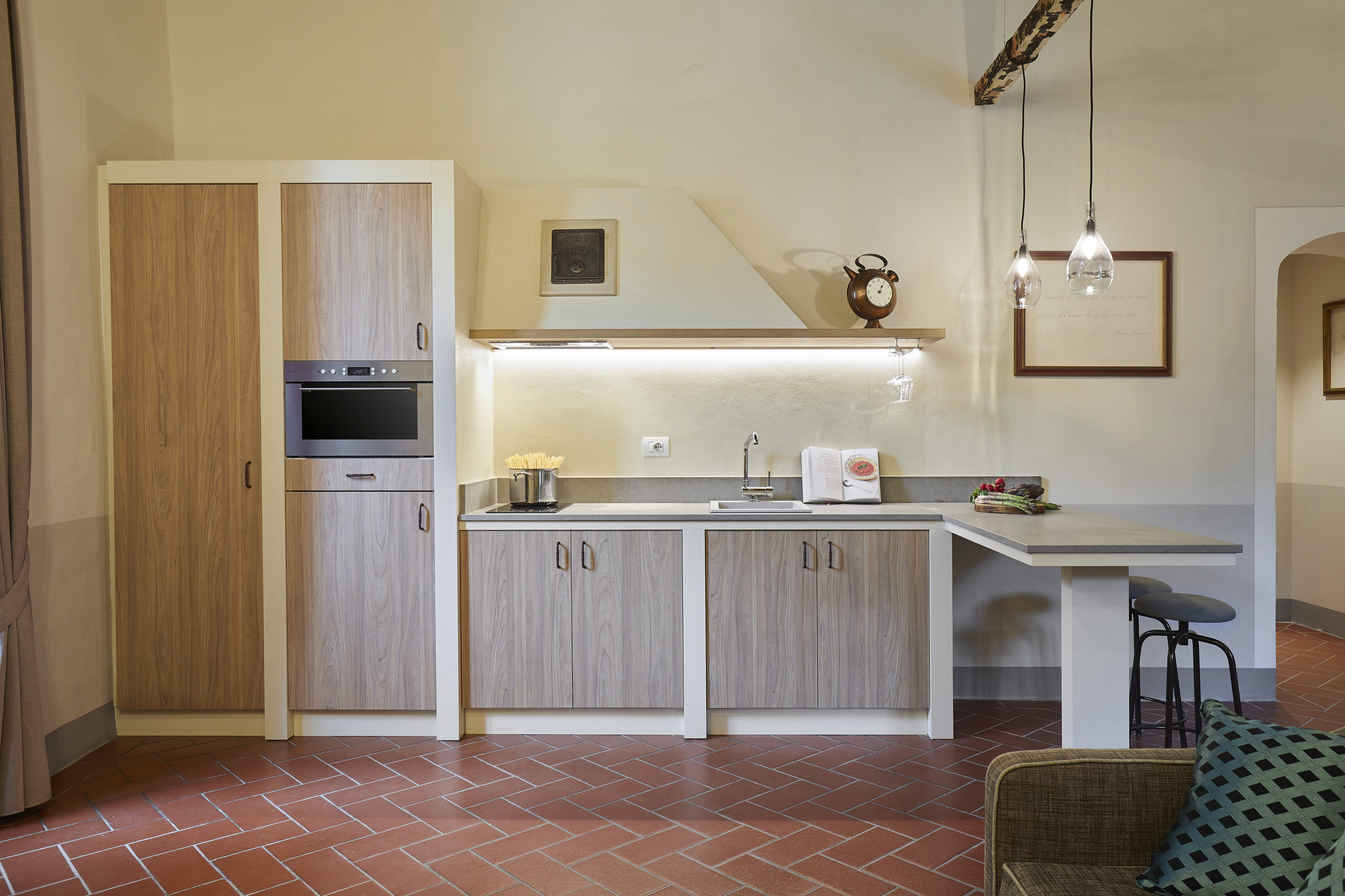 Light wood kitchen, built-in oven, sink, gray countertop, terracotta floor tiles.