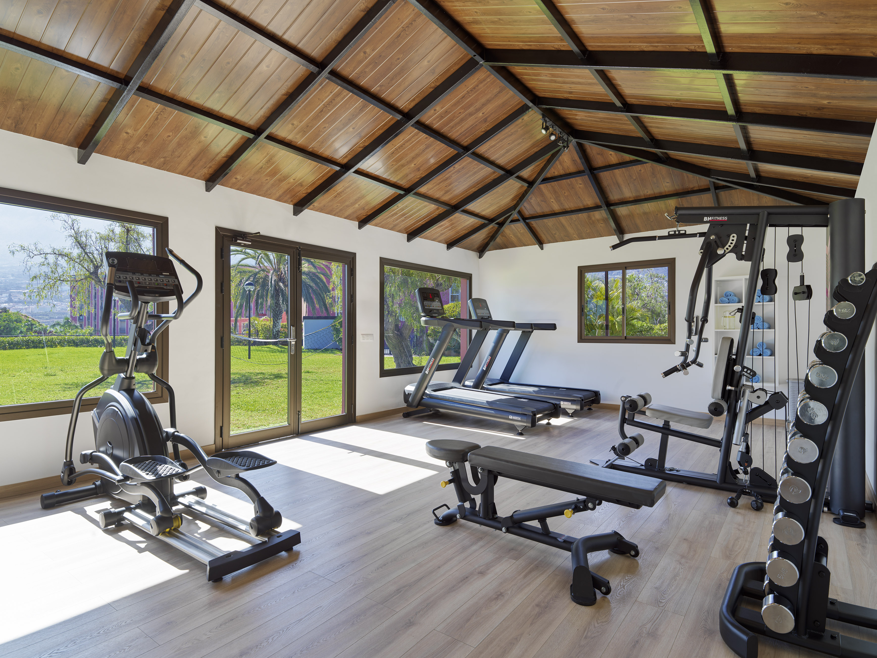 Modern gym with elliptical, treadmills, weights, and bright garden views.