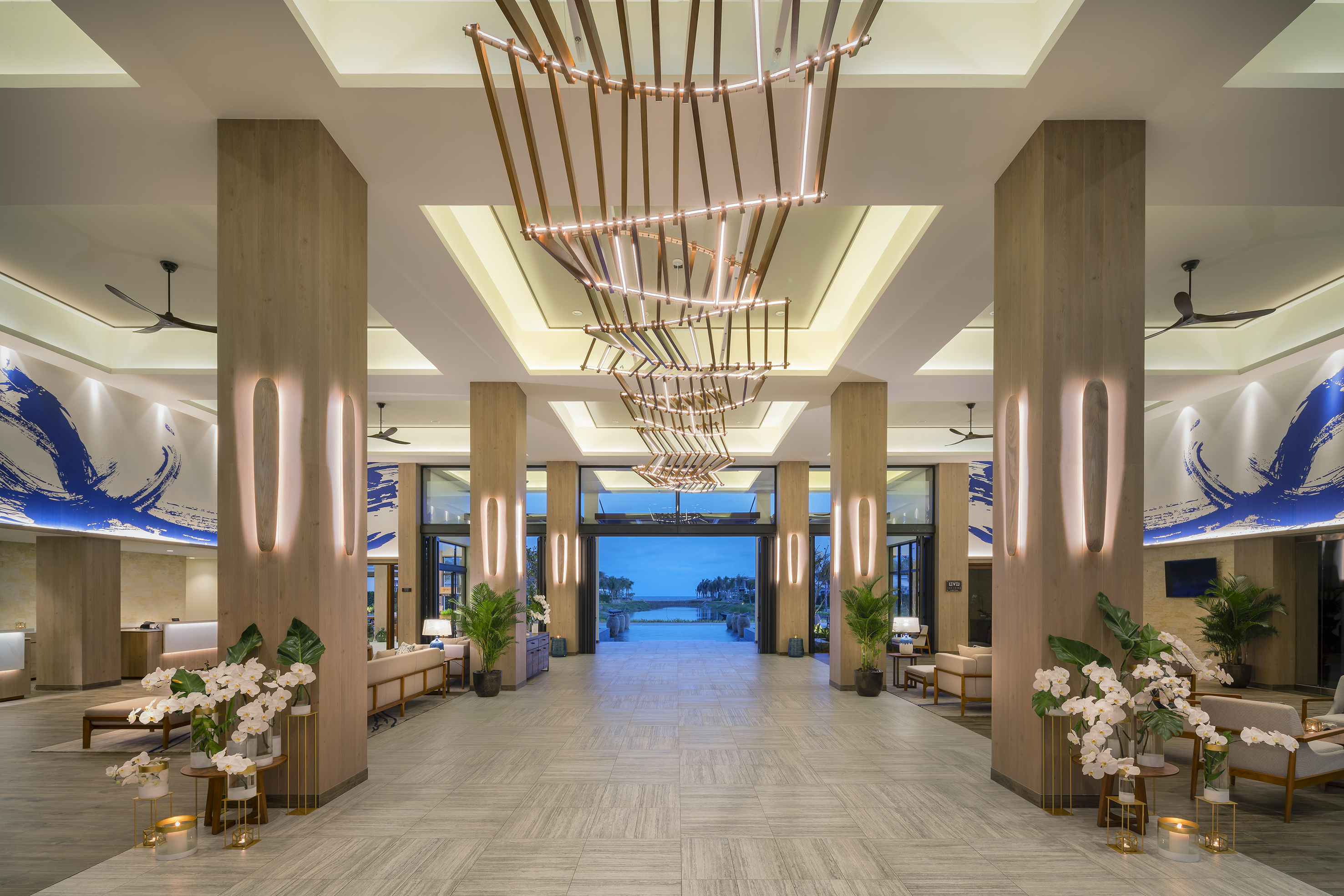 Modern hotel lobby with chandelier, wood details, and outdoor water view.