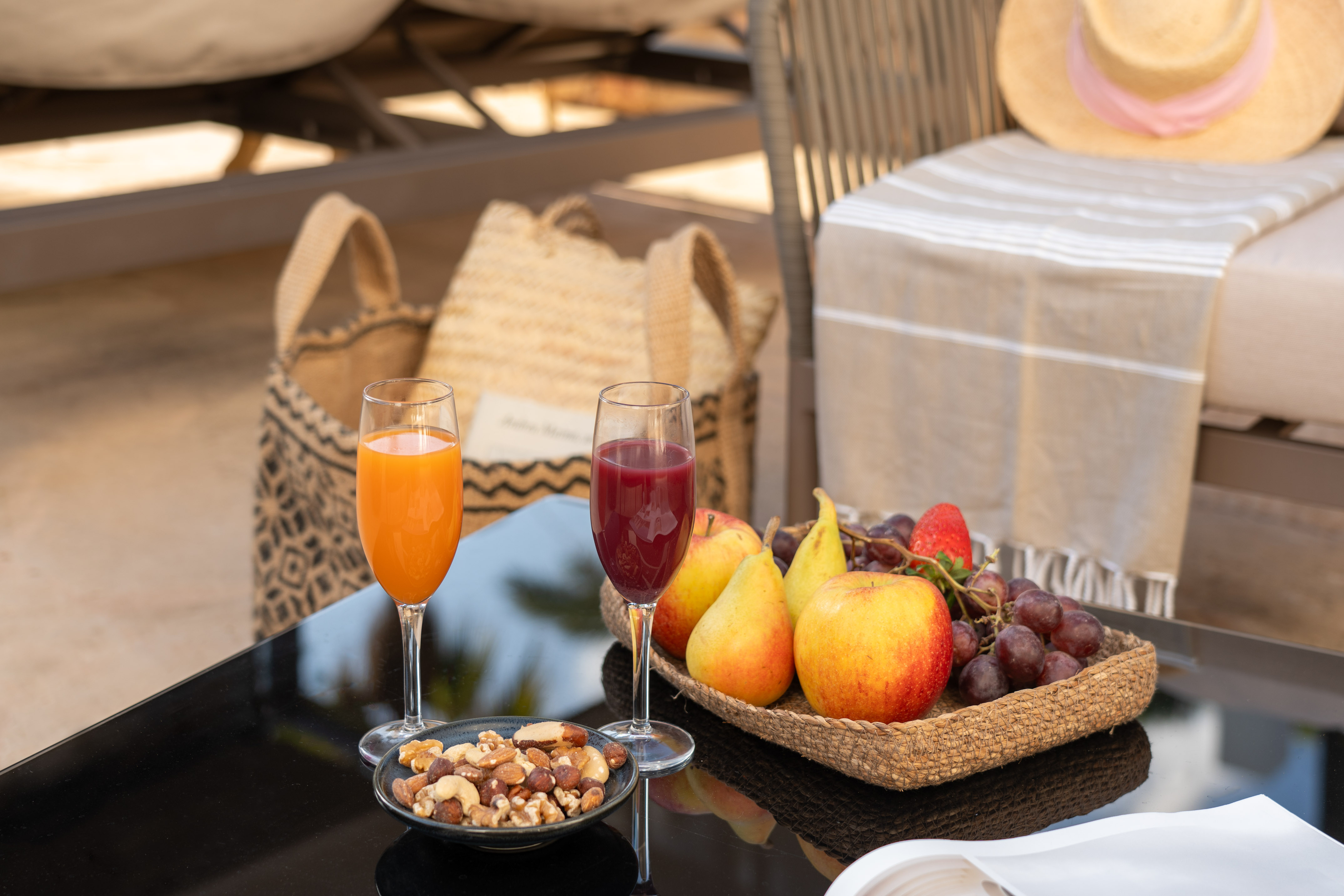 Healthy poolside snacks: fruit, nuts, and juices on a black table.