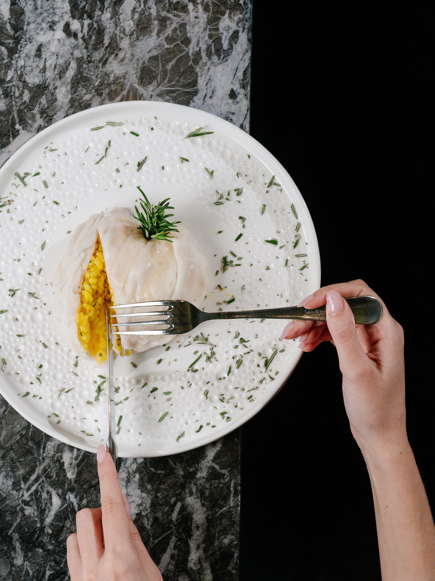 Hands cutting a savory stuffed roll with yellow rice and rosemary on a white plate.