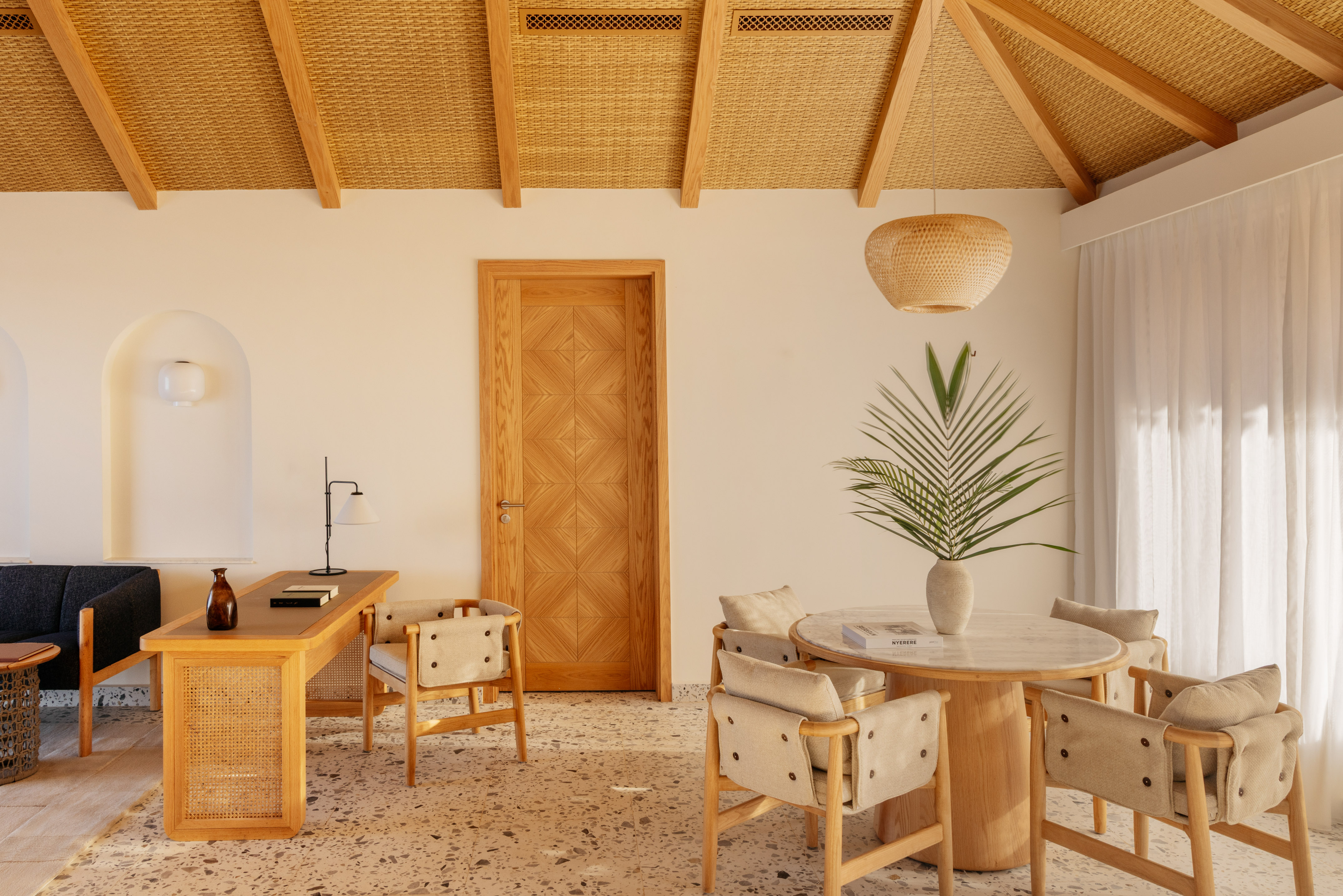 Woven ceiling interior with wooden desk, dining area, and terrazzo floor.
