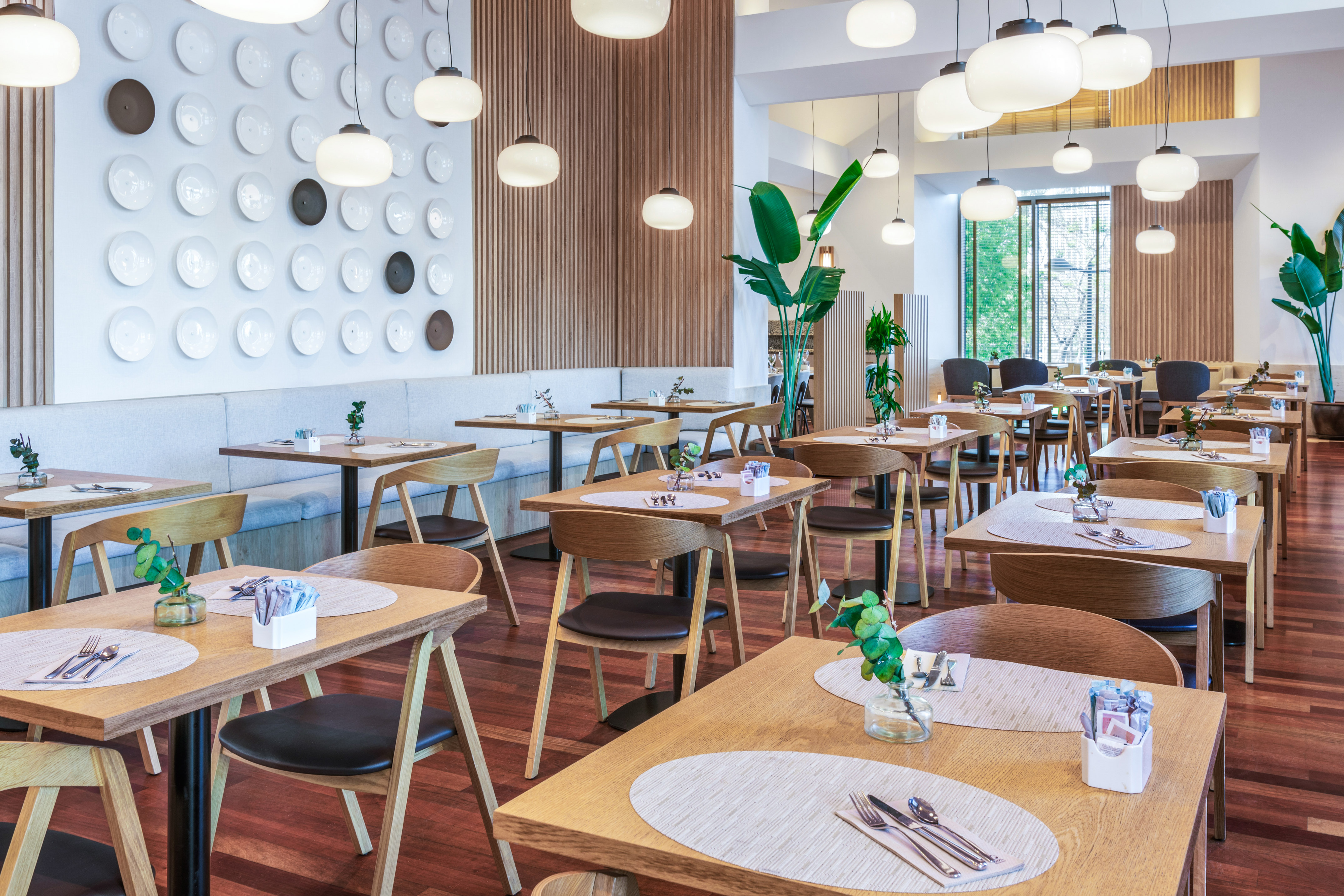 Chic restaurant interior with wooden tables, banquette, pendant lights, plate decor.
