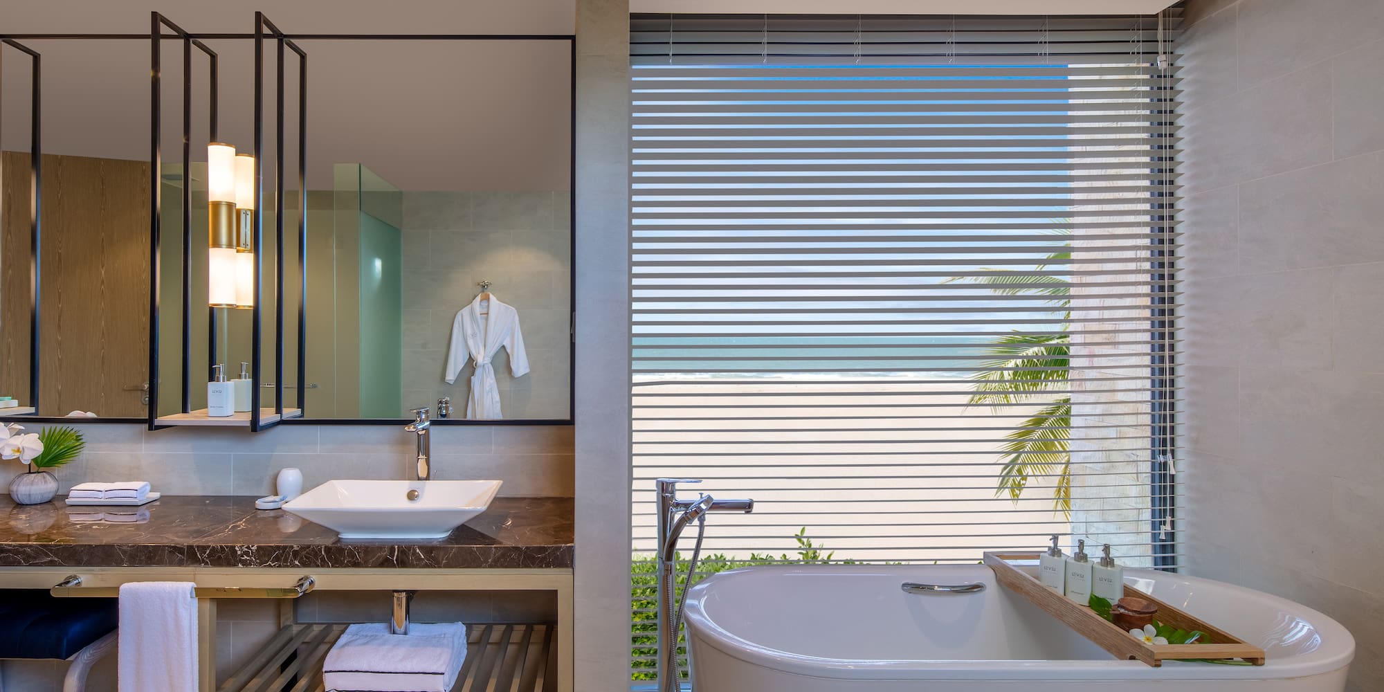 Oceanfront luxury bathroom with freestanding tub, modern vanity, and beach view.