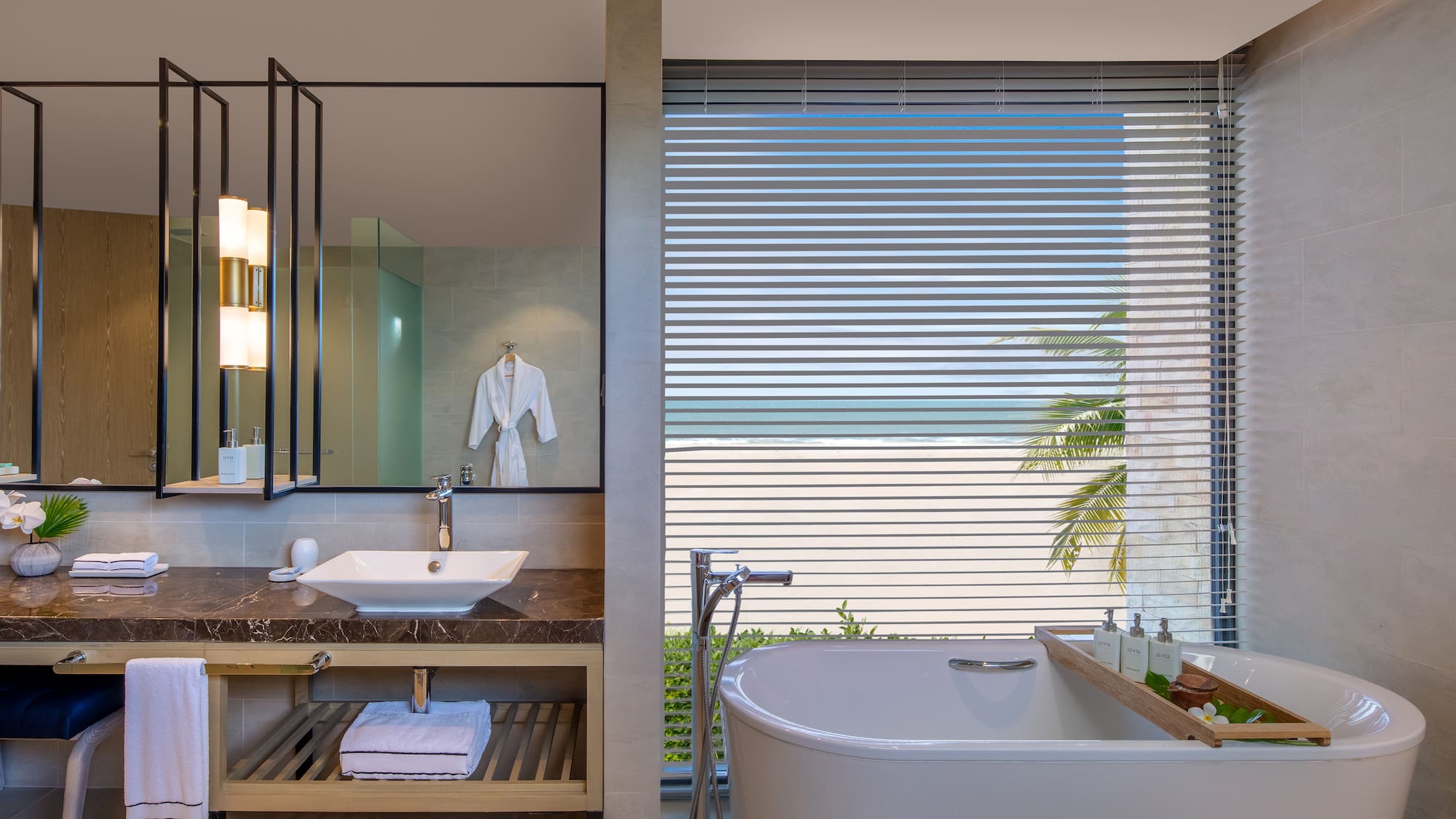 Oceanfront luxury bathroom with freestanding tub, modern vanity, and beach view.