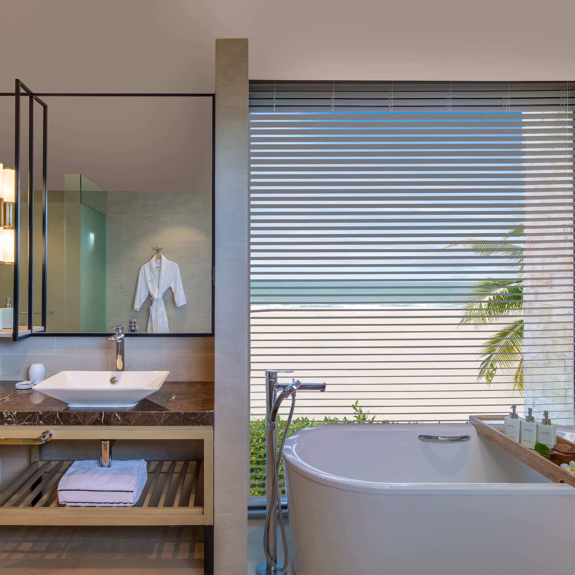 Oceanfront luxury bathroom with freestanding tub, modern vanity, and beach view.