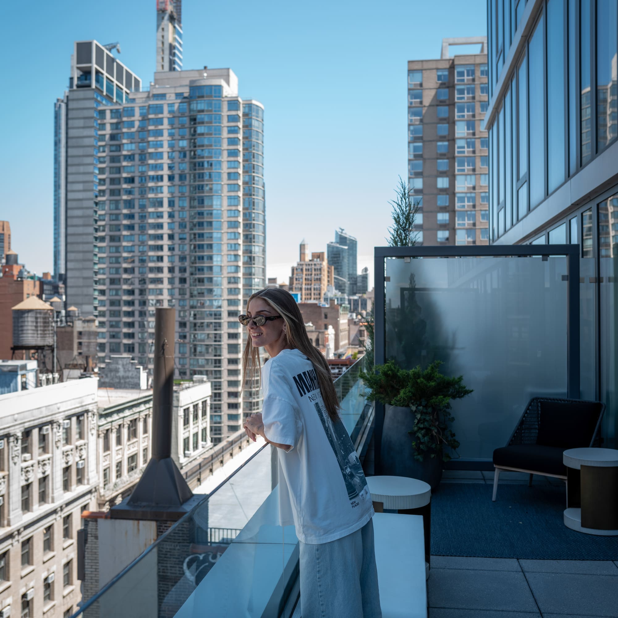 Smiling woman on modern city balcony, overlooking urban skyline and buildings.