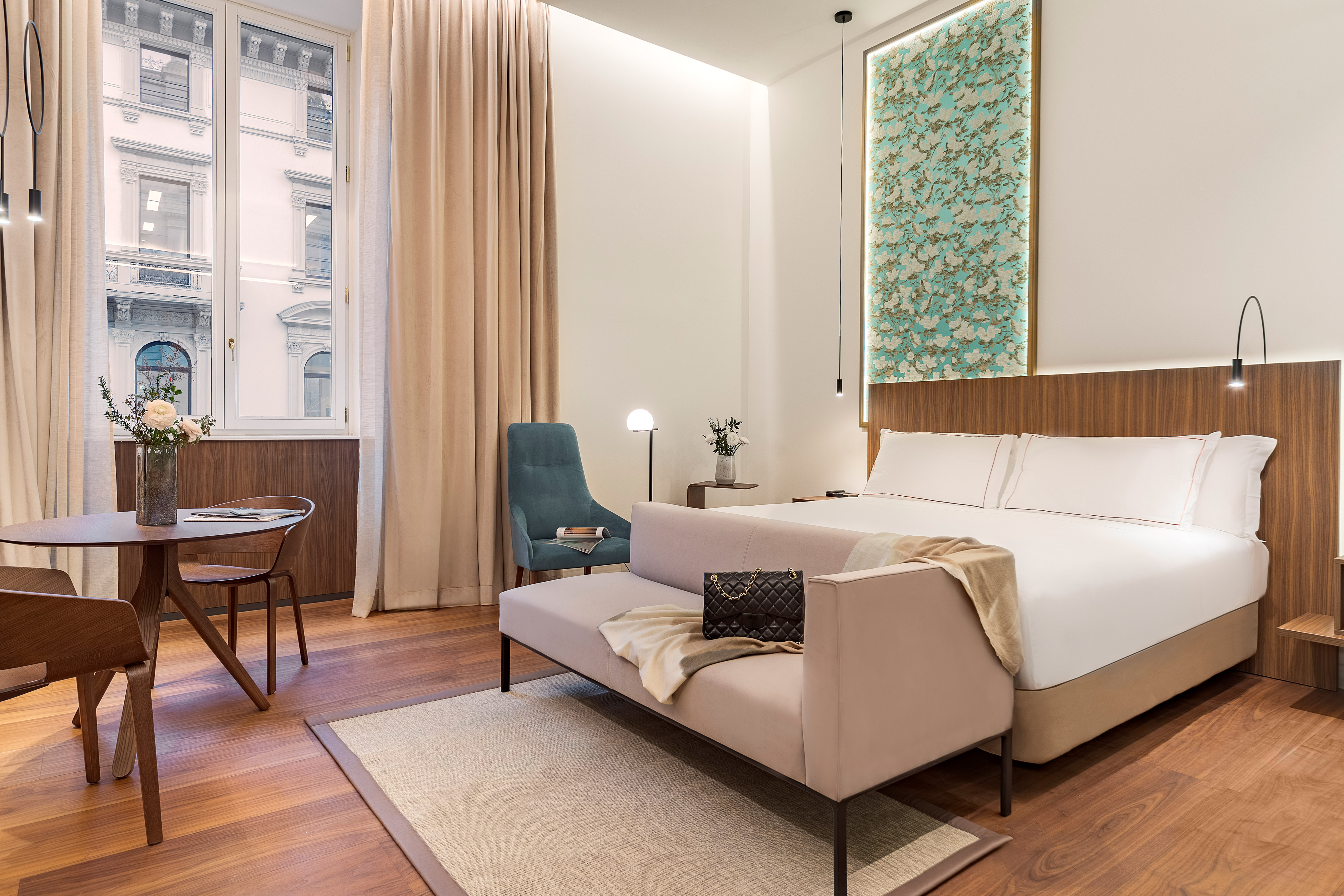 Modern hotel suite with king bed, dining area, chaise lounge, and window.