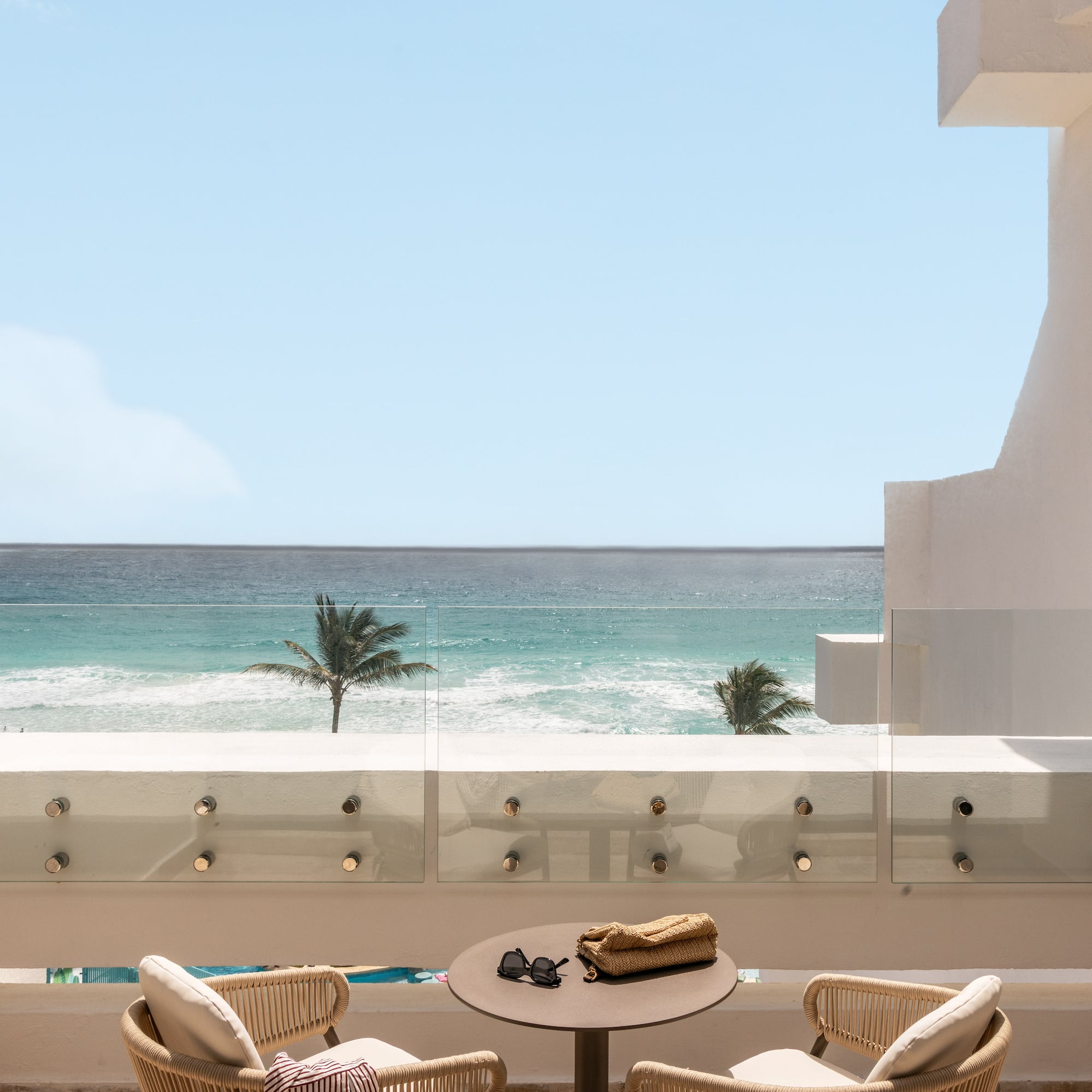 Oceanfront balcony with palm trees, modern seating, and clear blue water view.