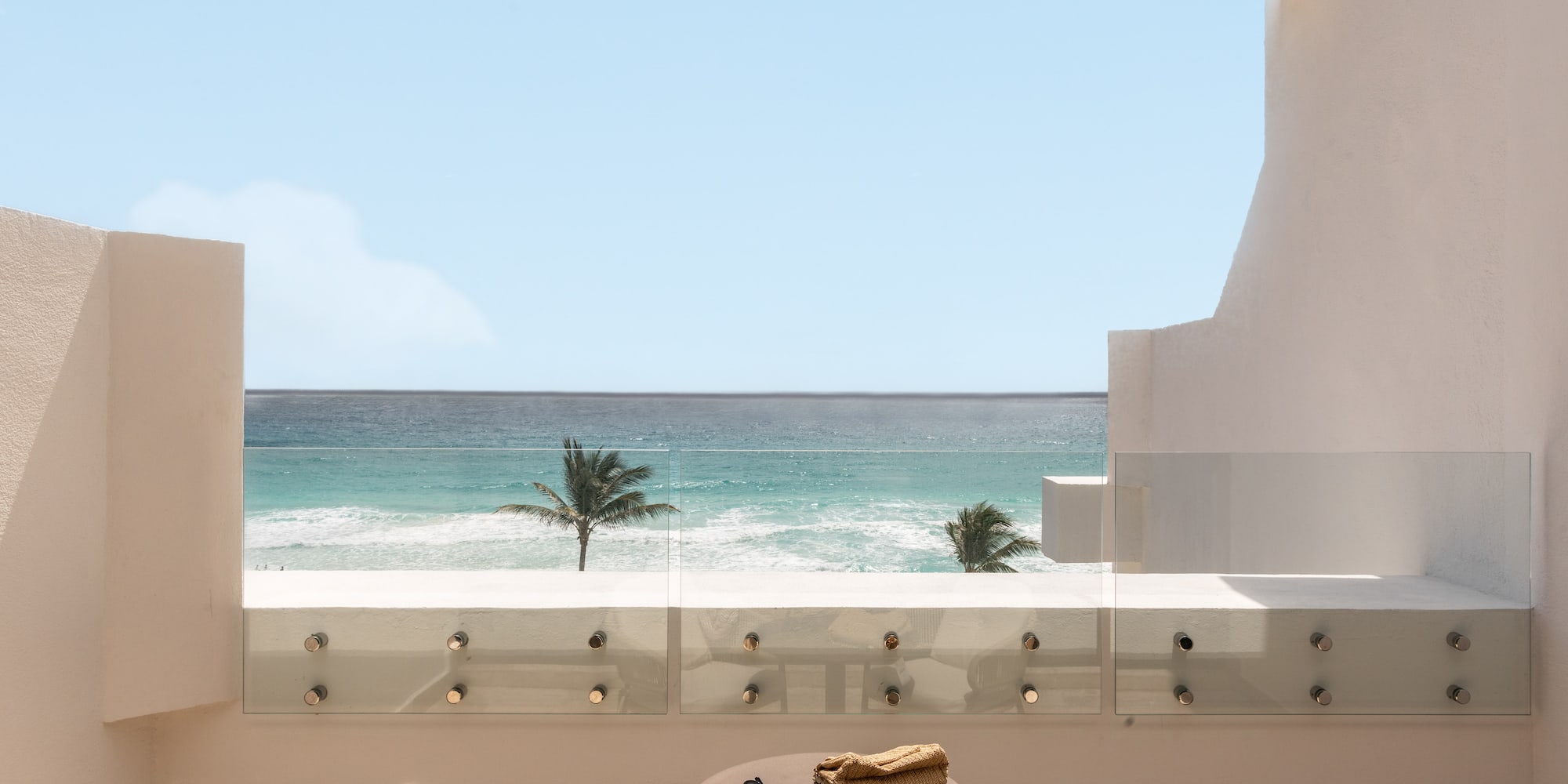 Beachfront balcony with ocean view, palm trees, and outdoor seating.