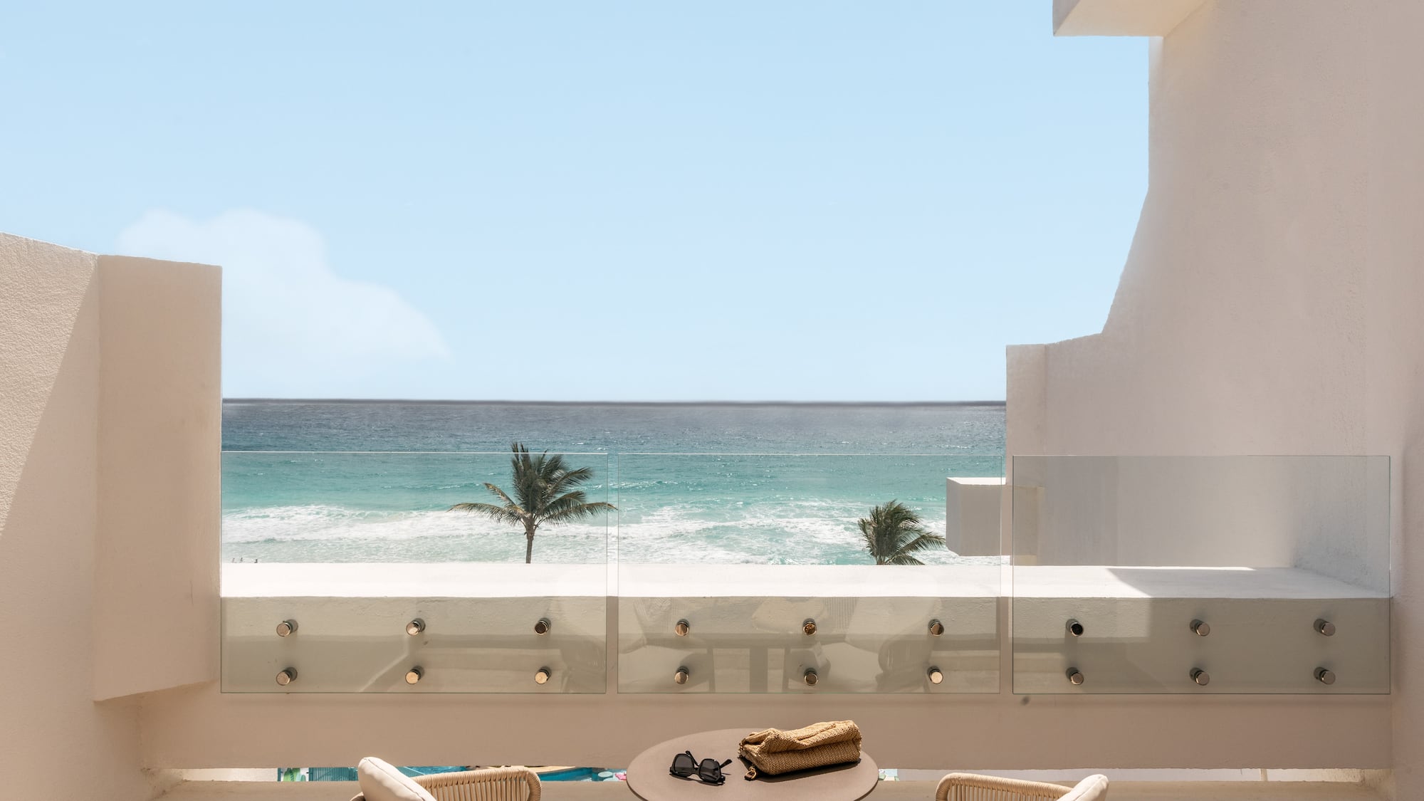 Beachfront balcony with ocean view, palm trees, and outdoor seating.