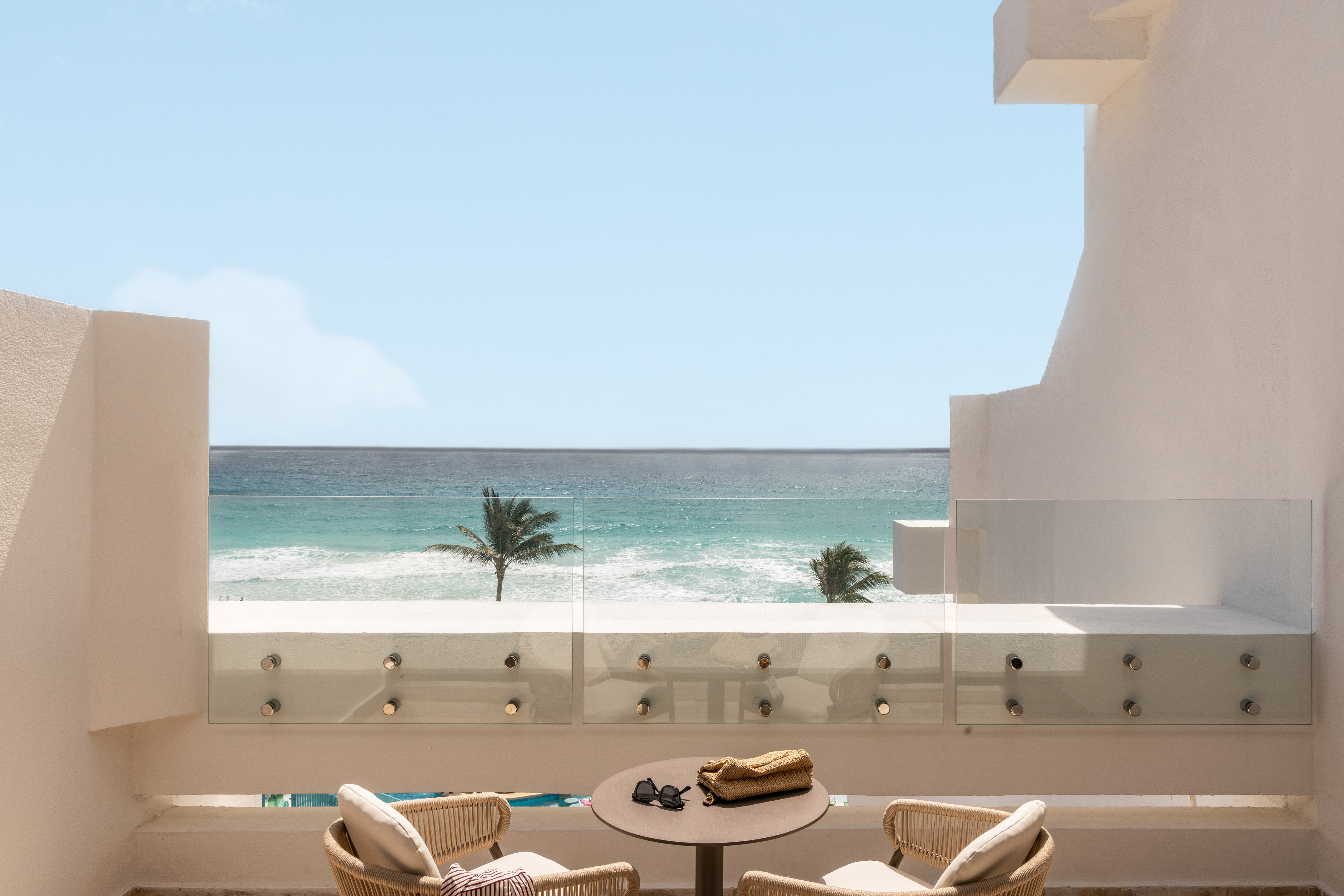 Beachfront balcony with ocean view, palm trees, and outdoor seating.