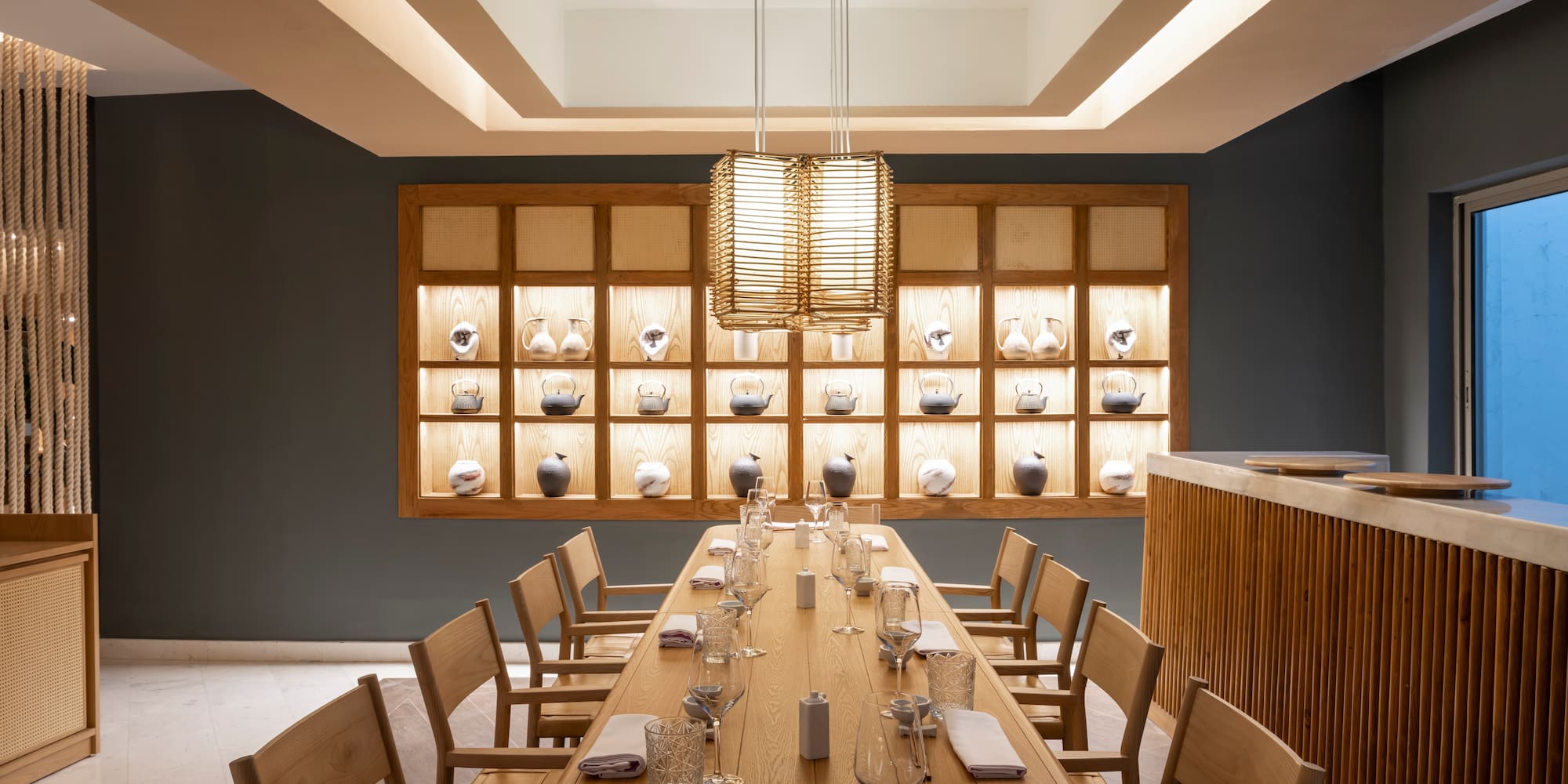 Modern Japanese dining room with long wooden table and illuminated tea ware.