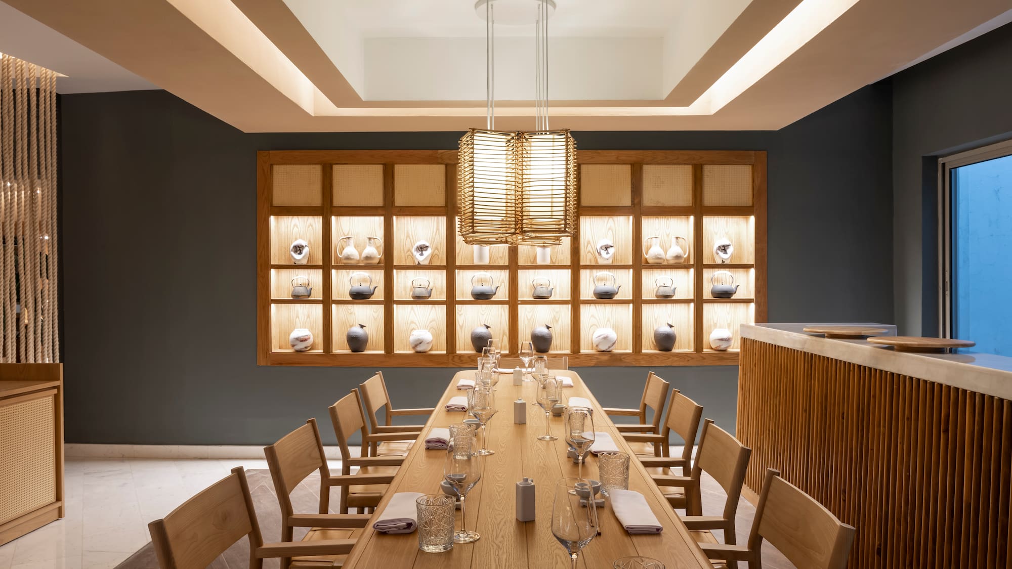 Modern Japanese dining room with long wooden table and illuminated tea ware.