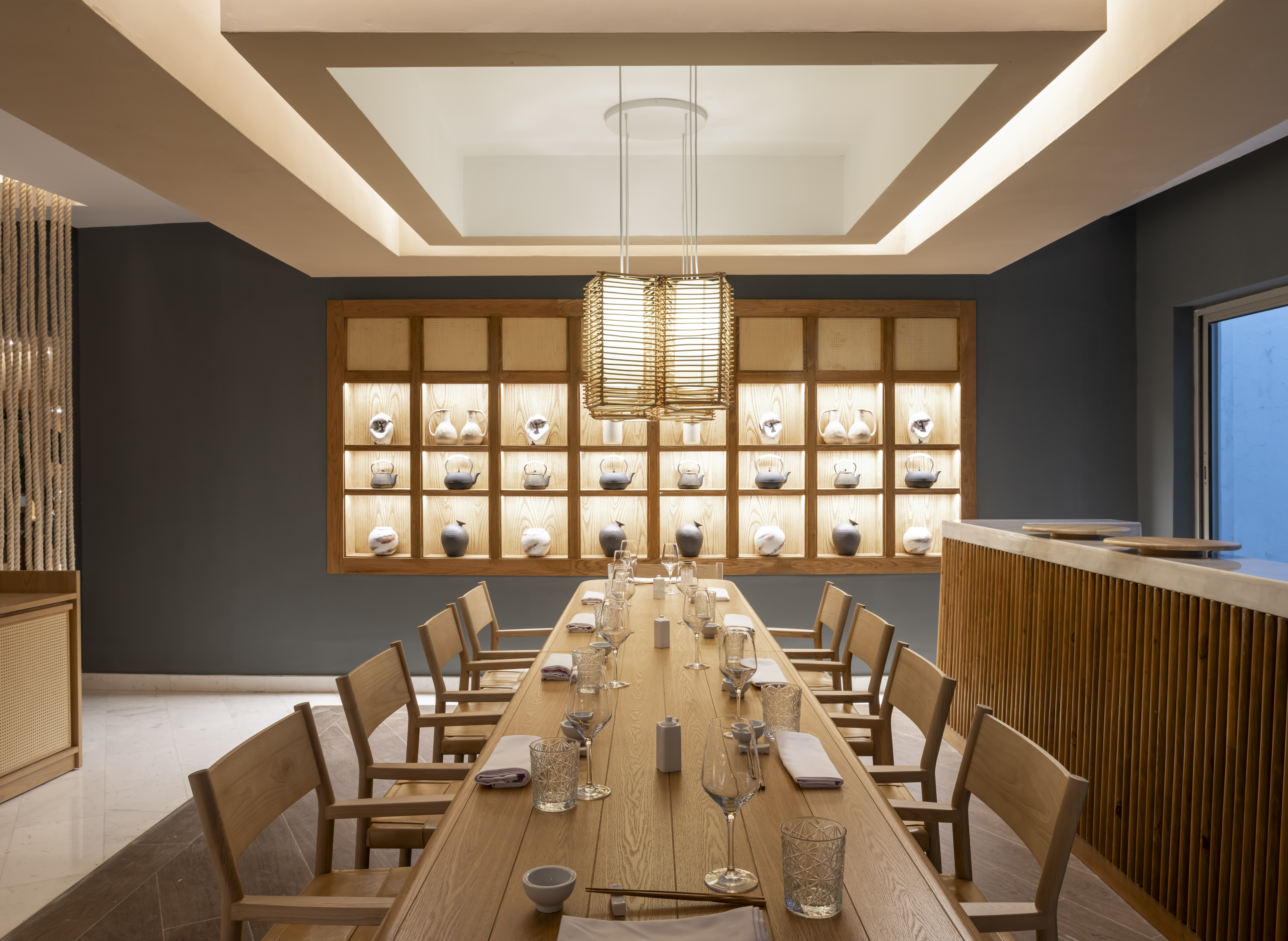 Modern Japanese dining room with long wooden table and illuminated tea ware.