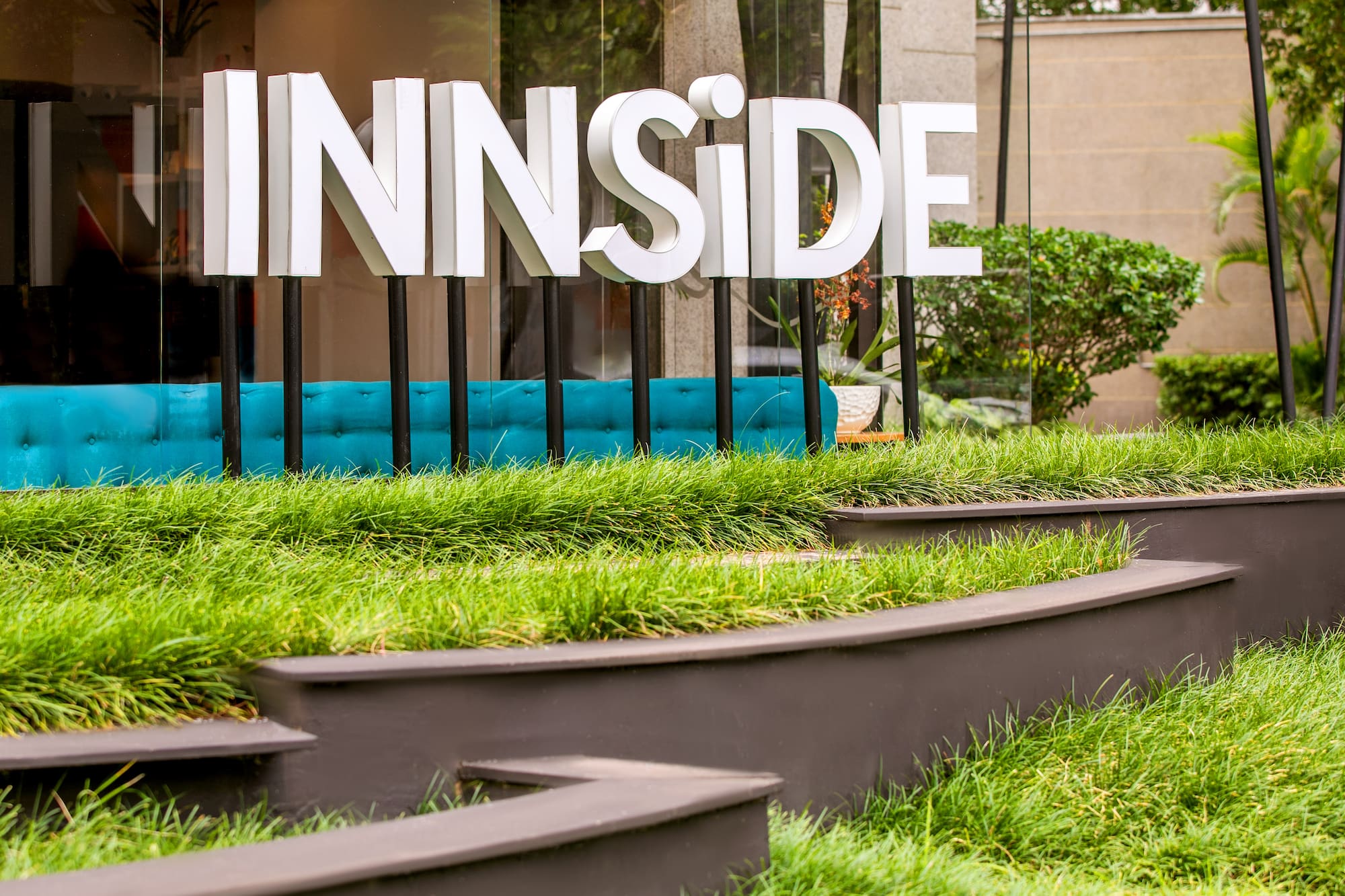 INNSIDE hotel sign with white letters, turquoise bench, and green tiered landscaping.