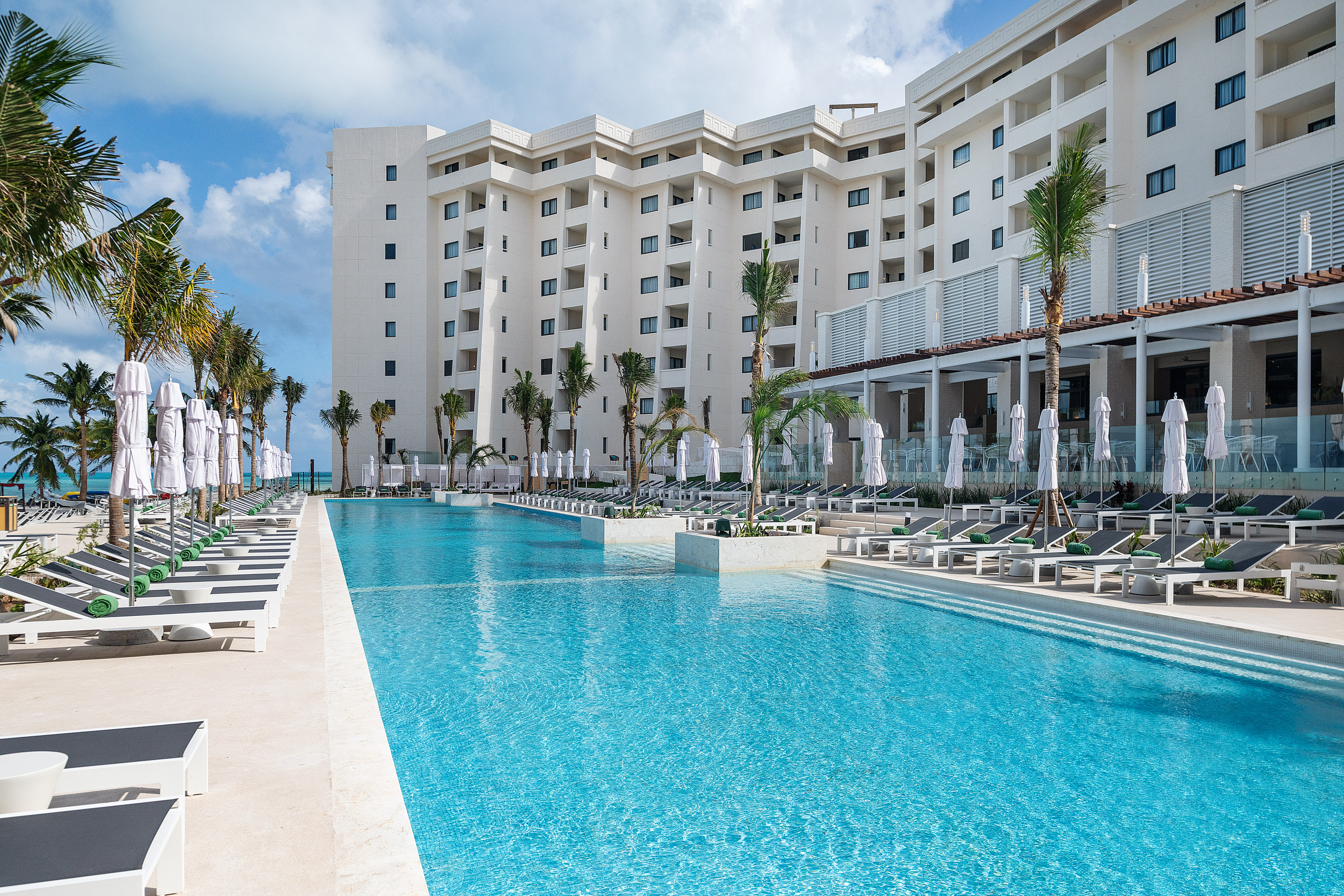 Luxury beach resort with large blue pool, palm trees, and lounge chairs.