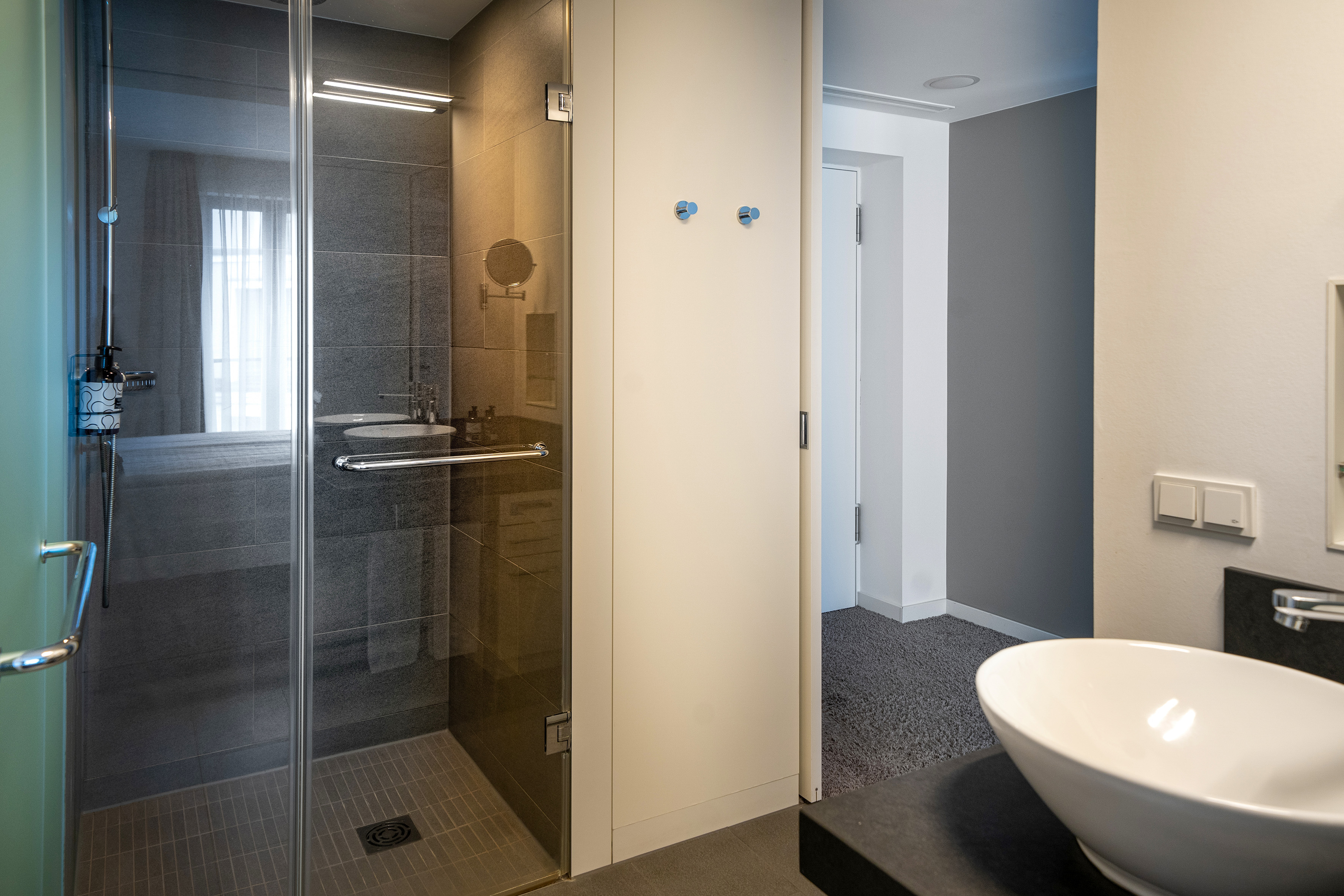 Modern hotel bathroom with walk-in glass shower, dark tiles, and vessel sink. - The INNSiDE Room - INNSiDE Dresden, Dresden