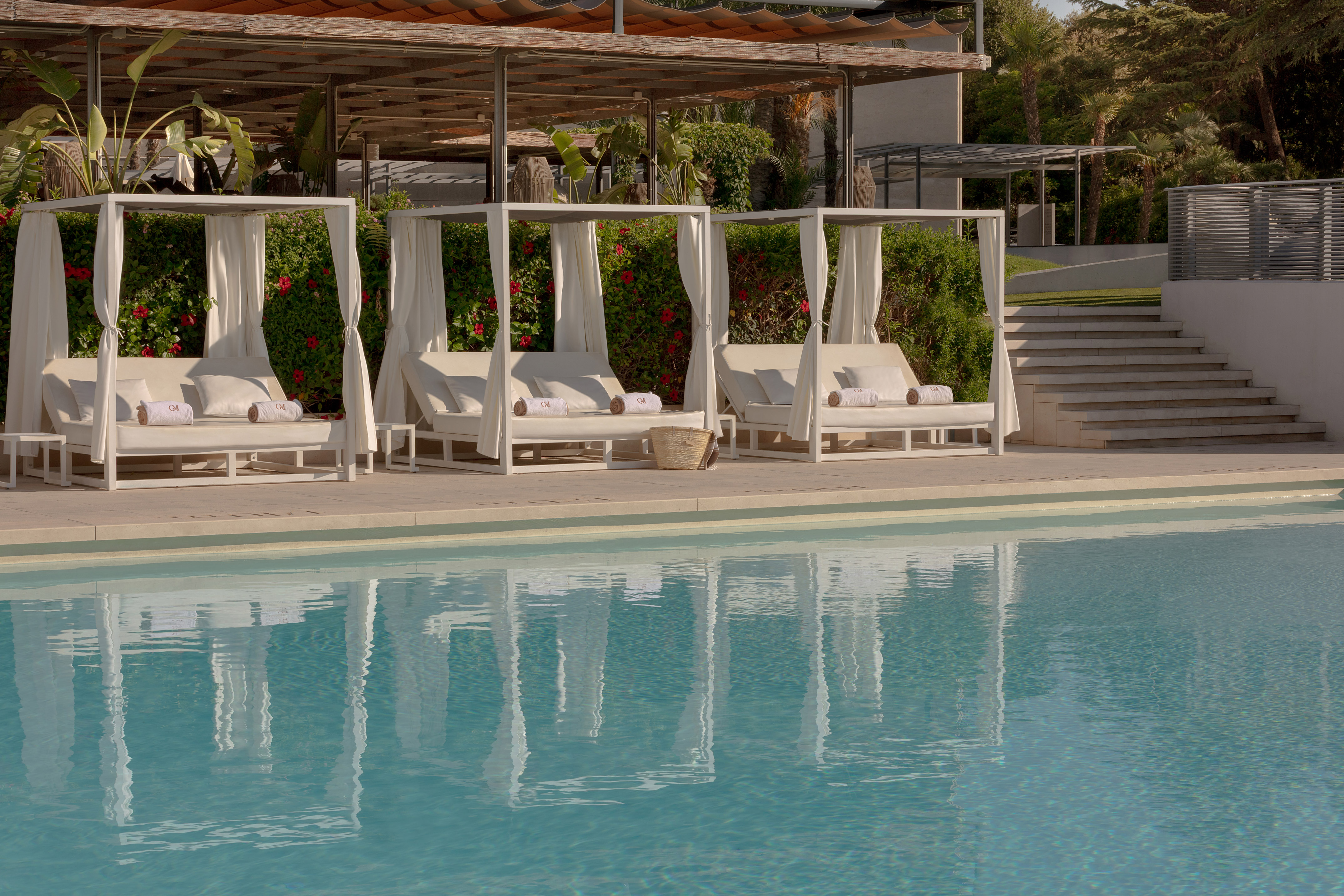 Three white poolside cabanas by a blue swimming pool with lush greenery.