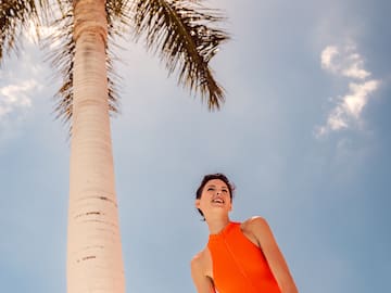 a woman in an orange dress standing next to a palm tree