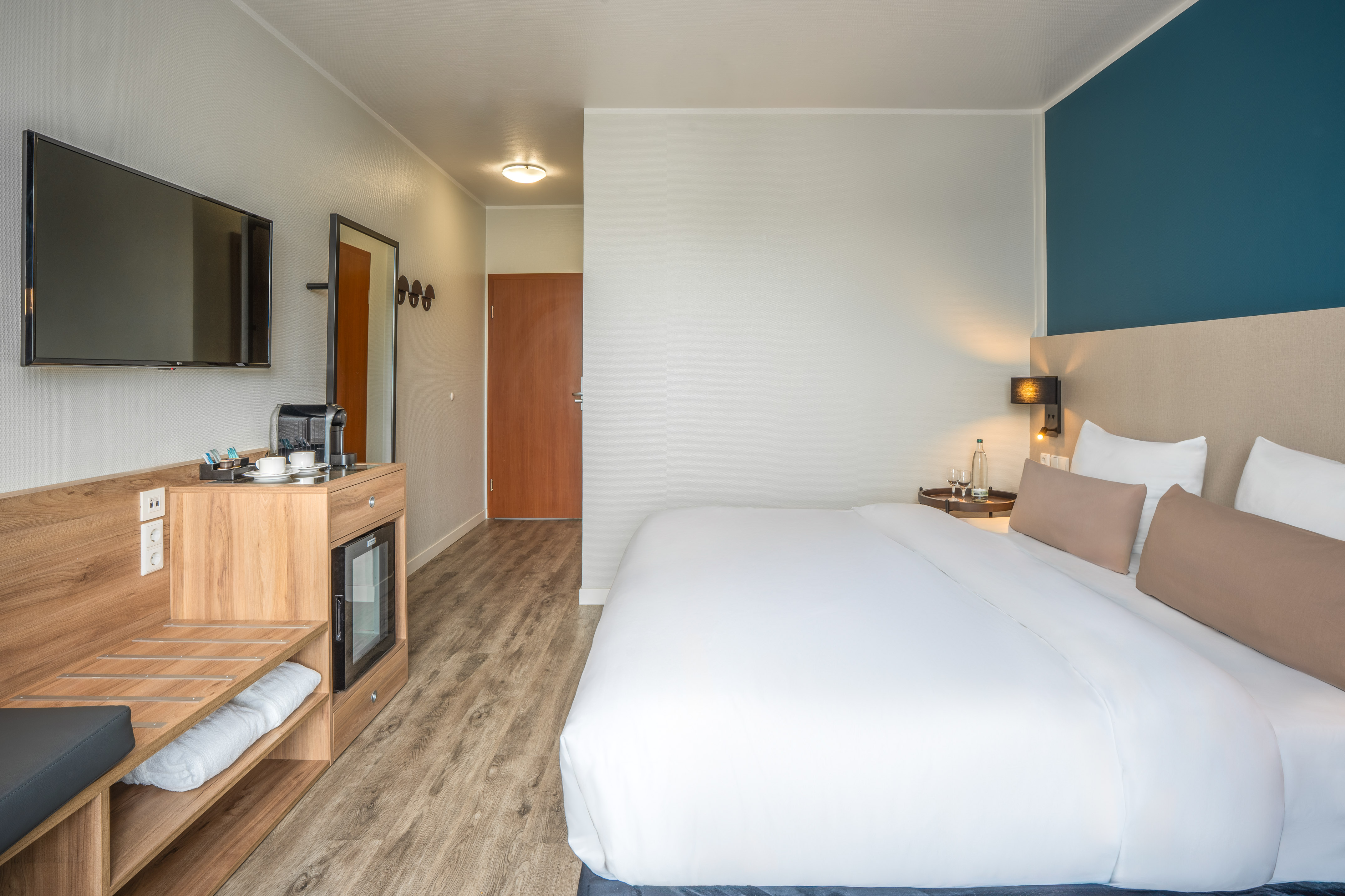 Modern hotel room with bed, TV, coffee station, and mini-fridge.