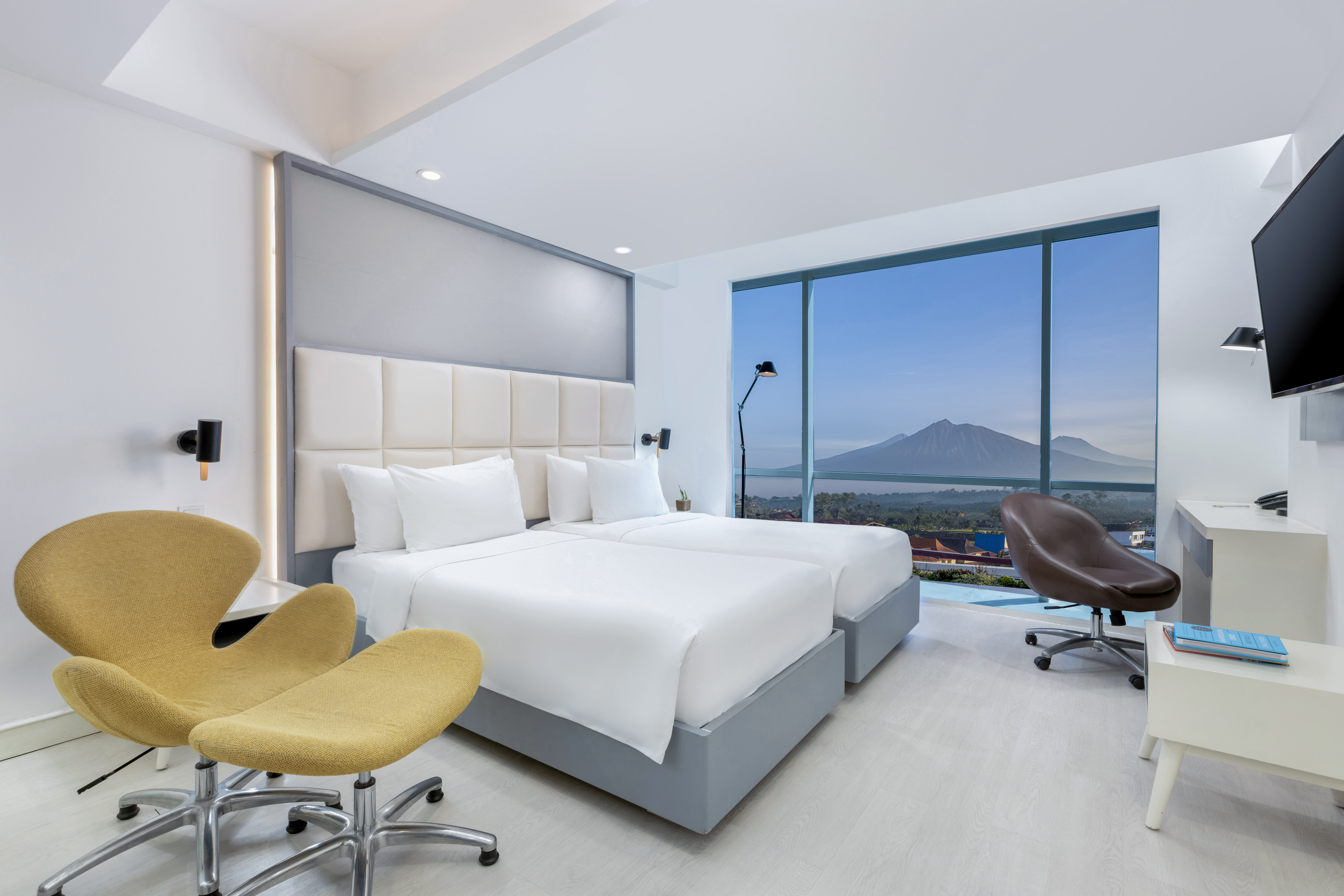 Modern hotel room with twin beds, mountain view from large window.