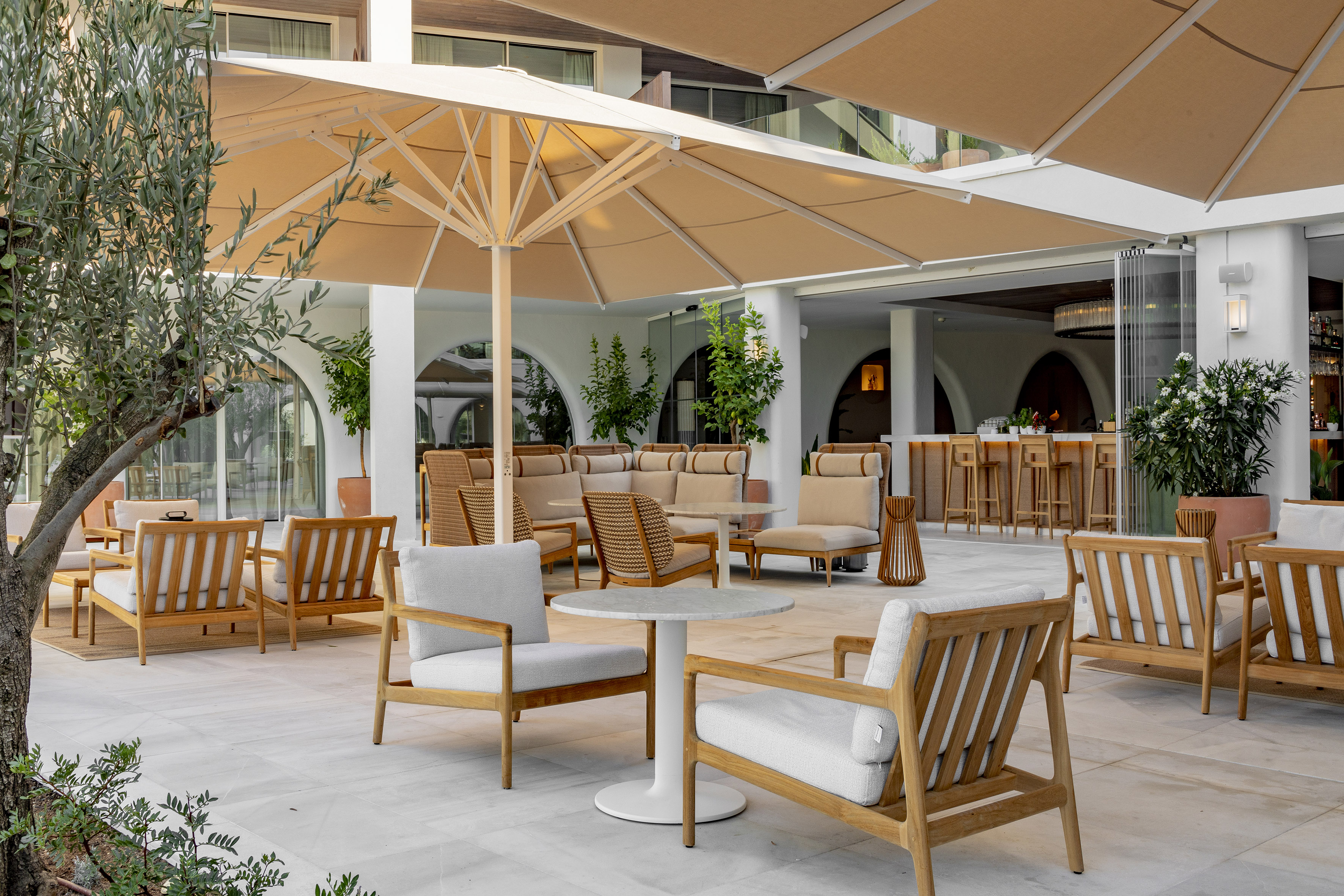 Outdoor hotel lounge patio with modern wood furniture, umbrellas, and bar.
