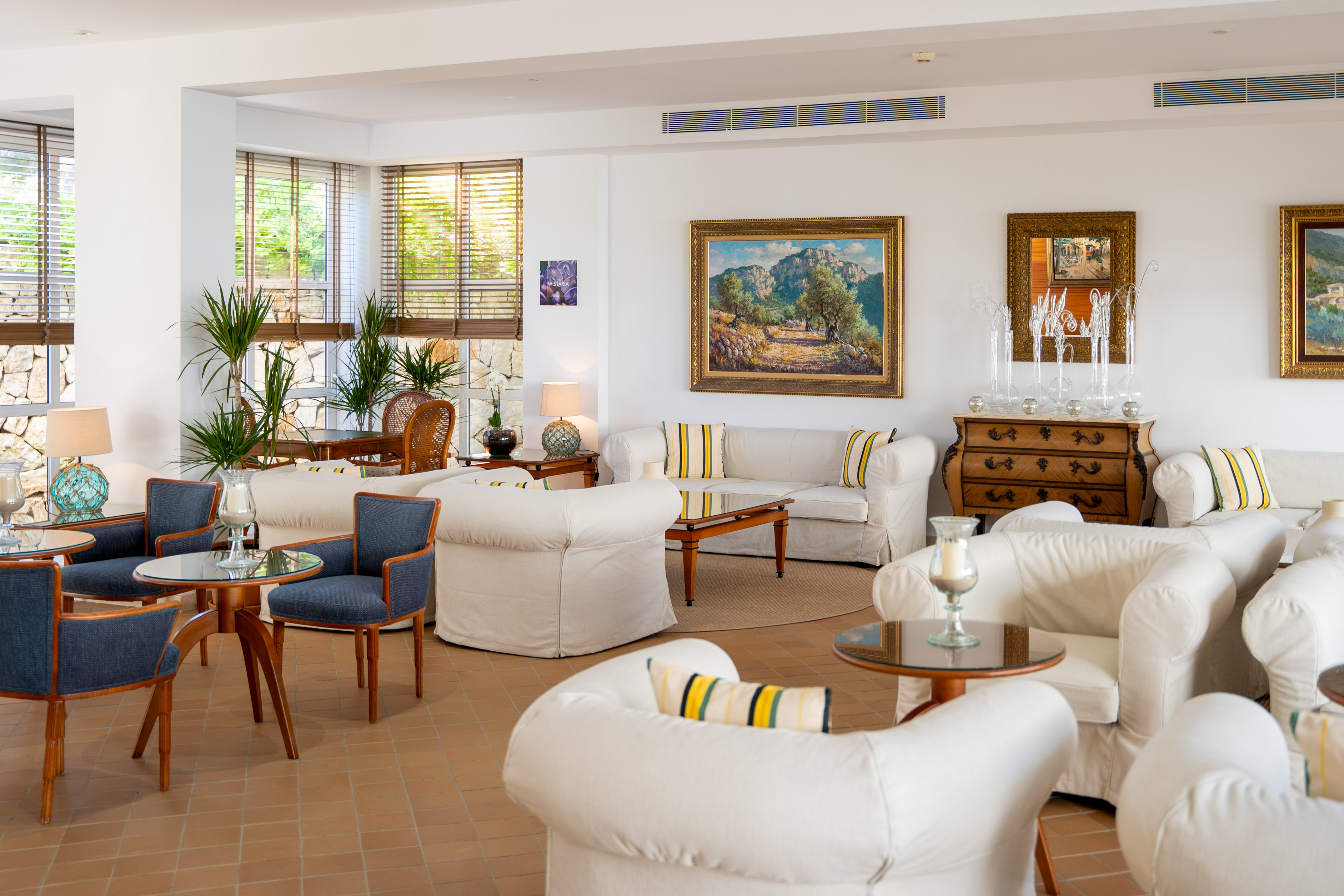 Bright hotel lounge with white sofas, landscape paintings, and potted plants.