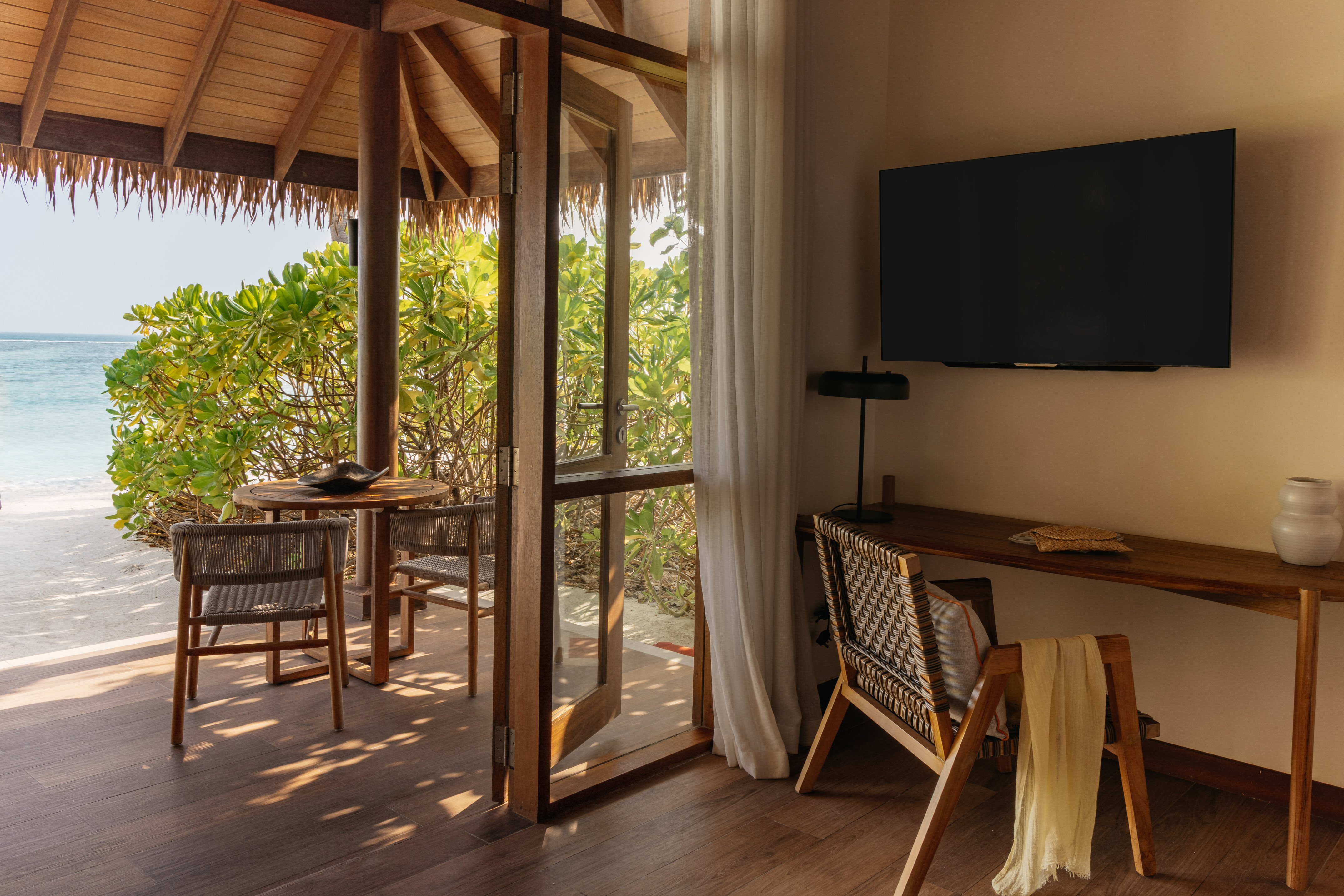 Beachfront villa room with thatched patio, ocean view, wooden furnishings, and TV.