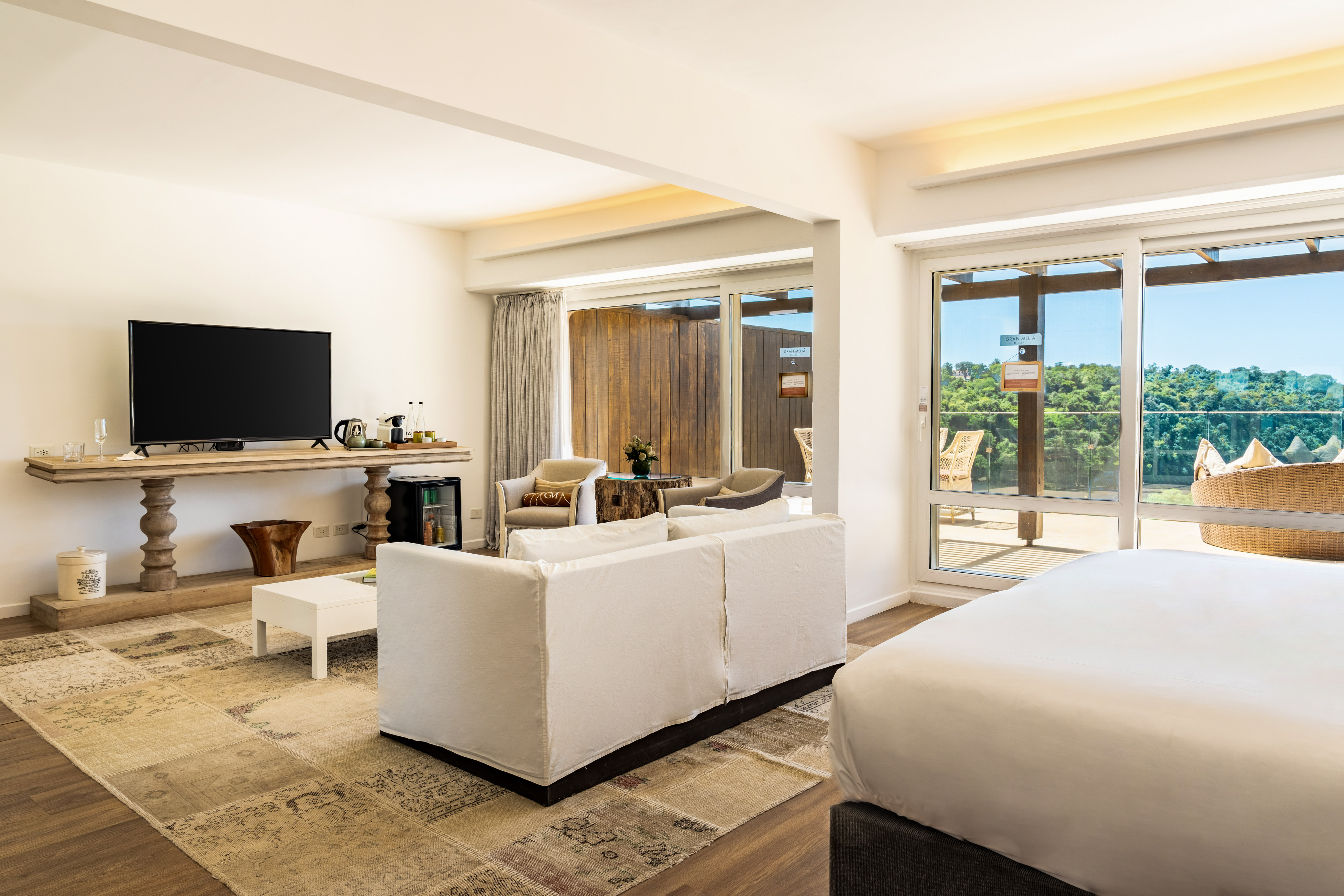 Spacious hotel suite living area with TV, sofa, and balcony view.