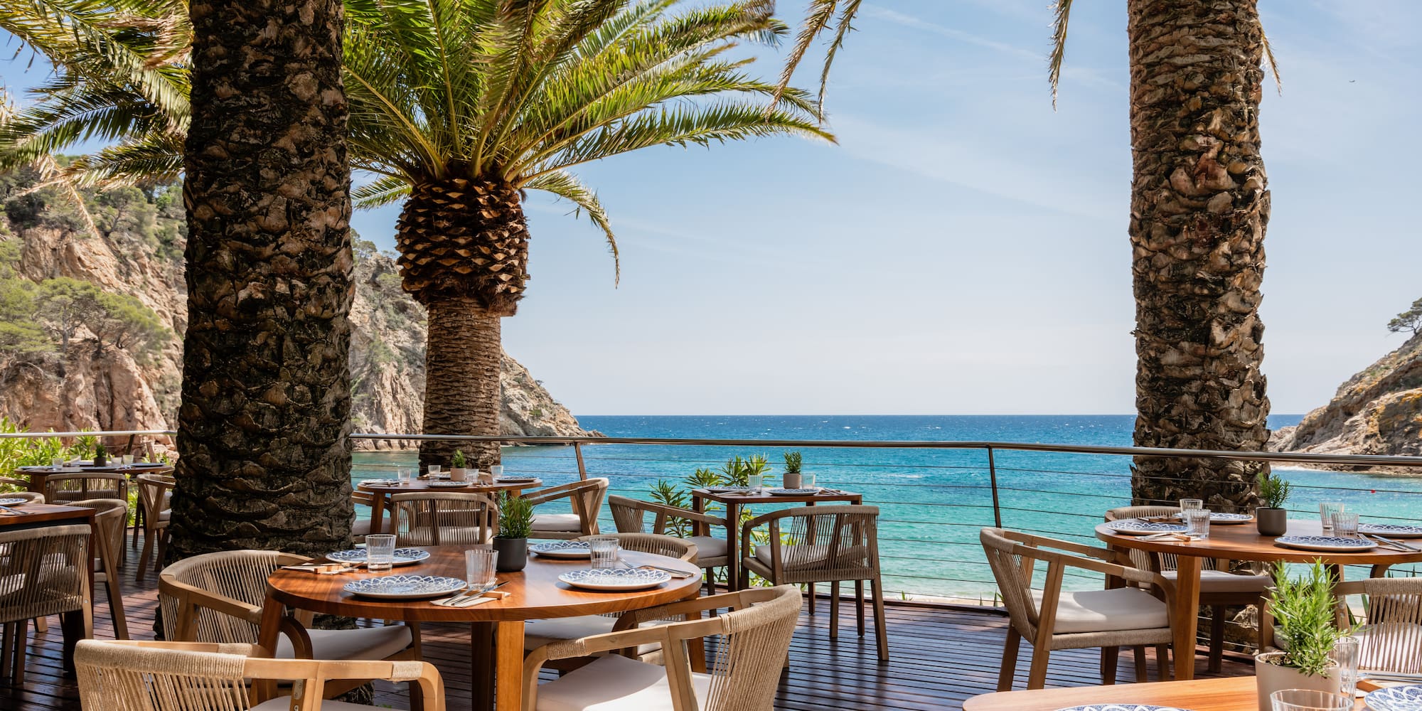 Tropical outdoor restaurant on a wooden deck with sea views and palm trees.