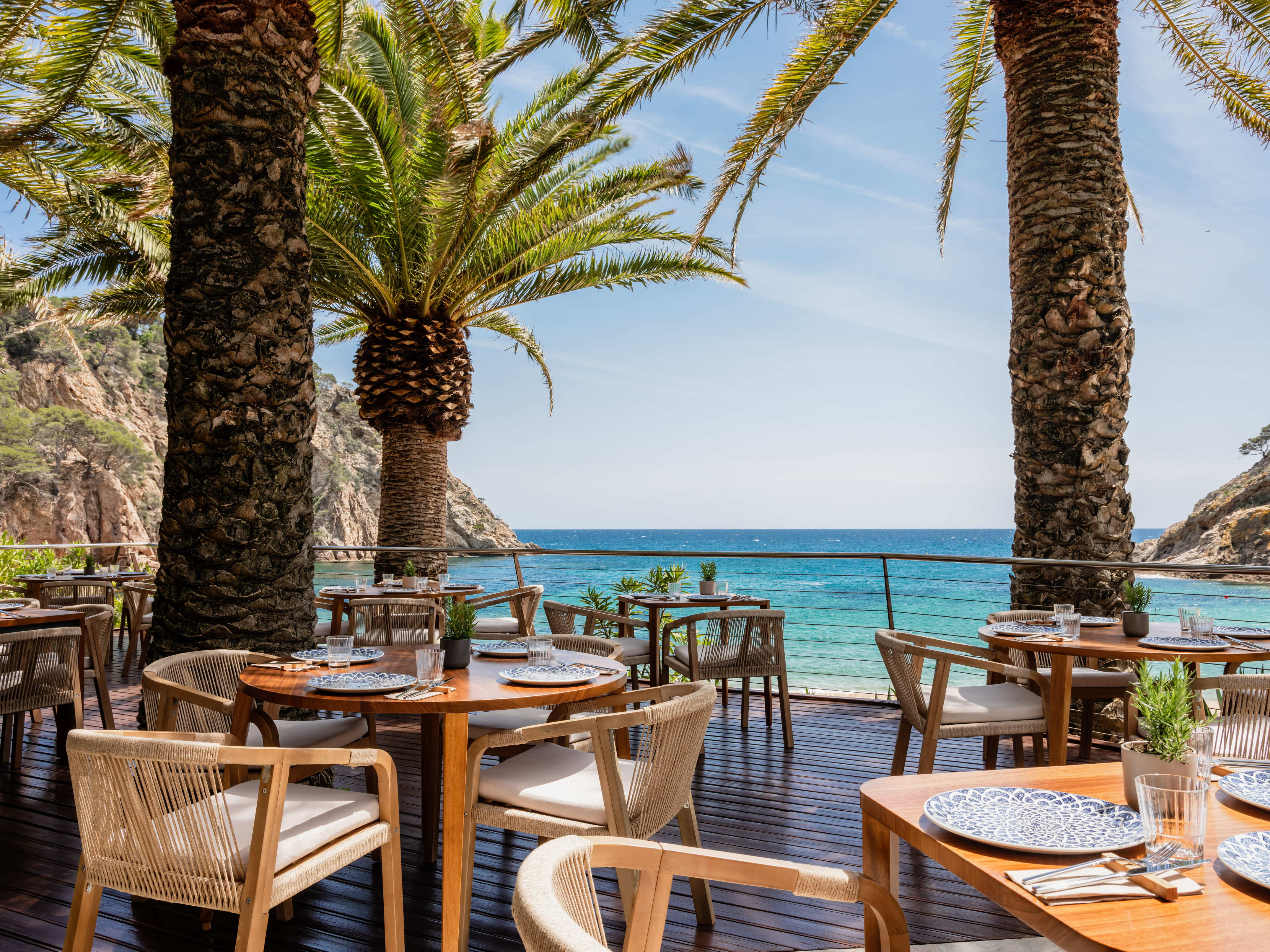 Tropical outdoor restaurant on a wooden deck with sea views and palm trees.