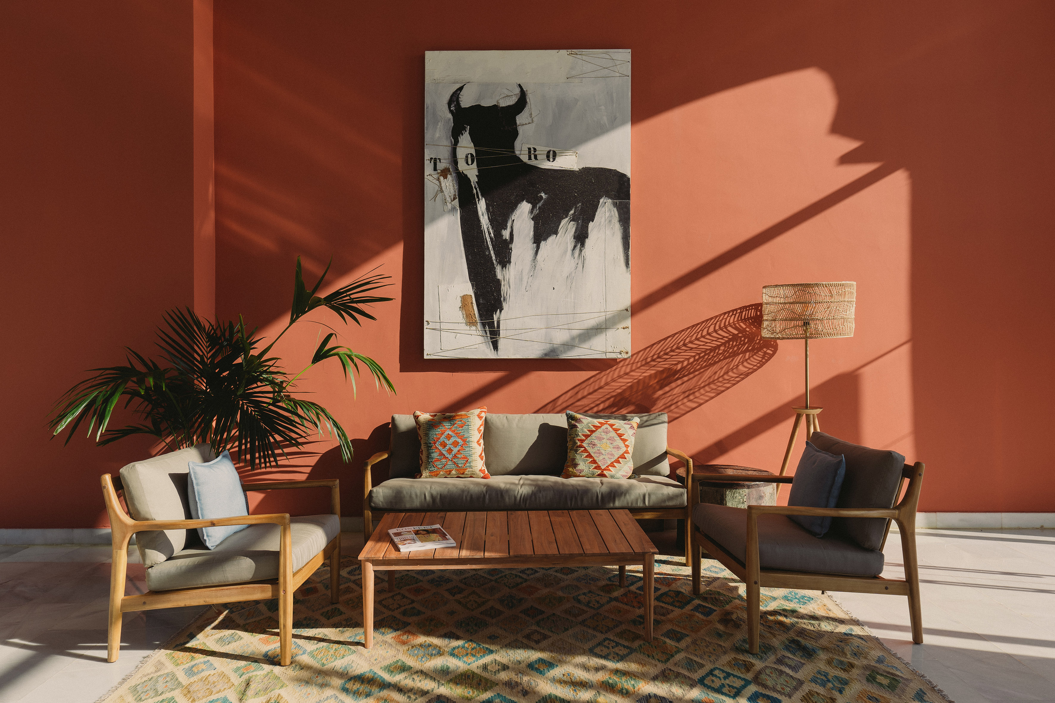Modern lounge with terracotta wall, Toro bull art, wooden sofa and armchairs.