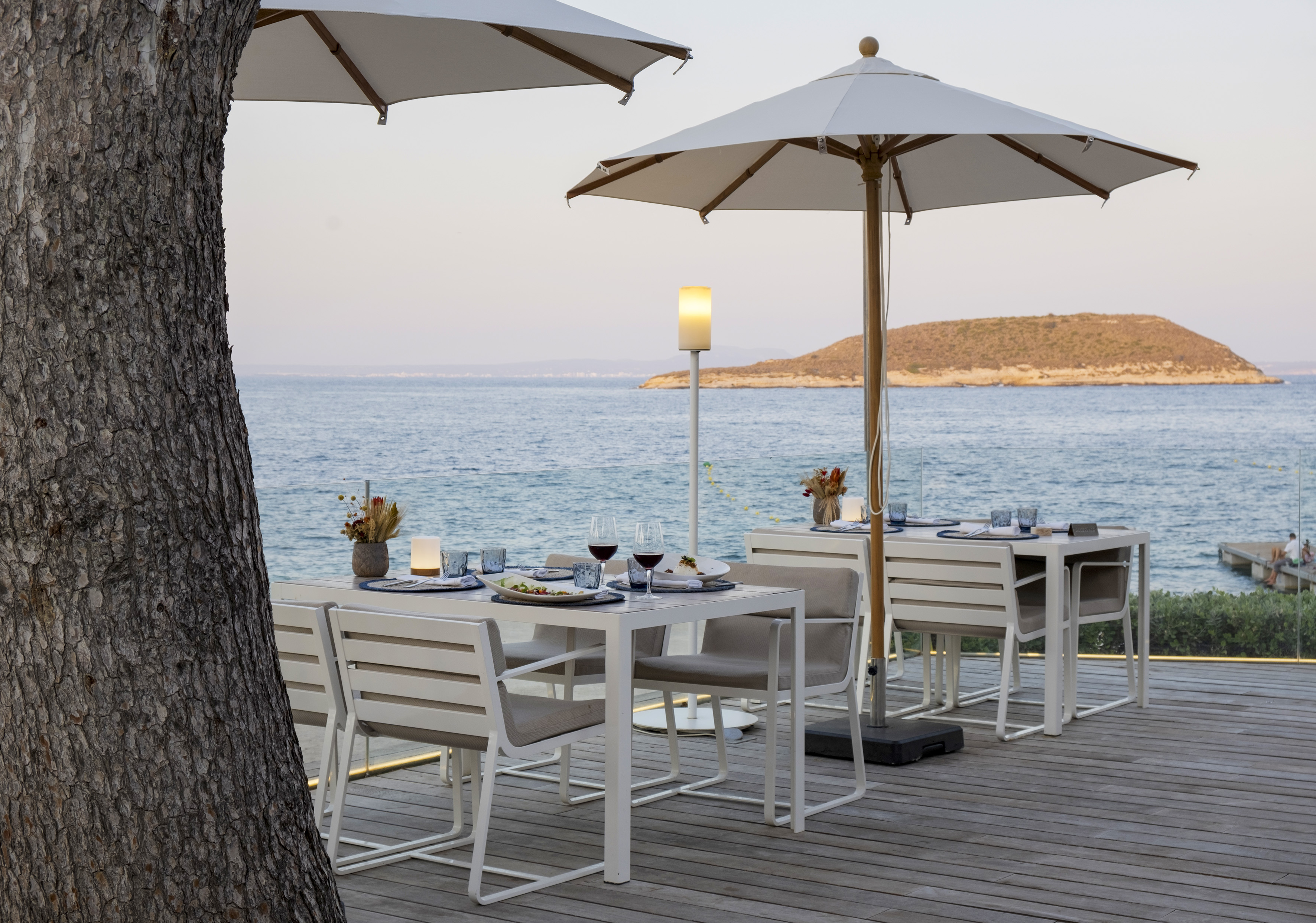 Outdoor dining tables on wooden deck with ocean view, distant island, and umbrellas.