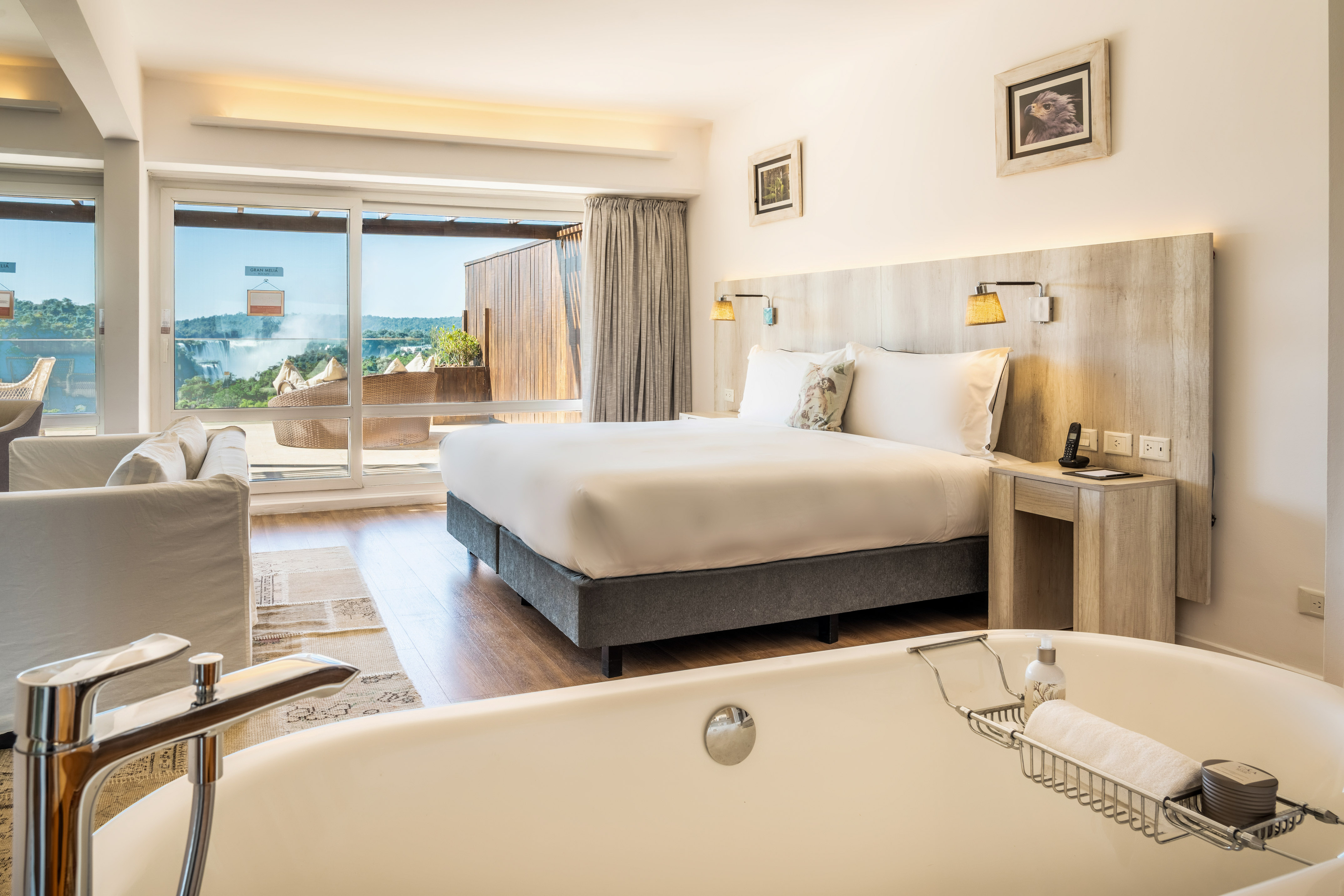 Hotel suite with modern bed, freestanding bathtub, and Iguazu Falls view.