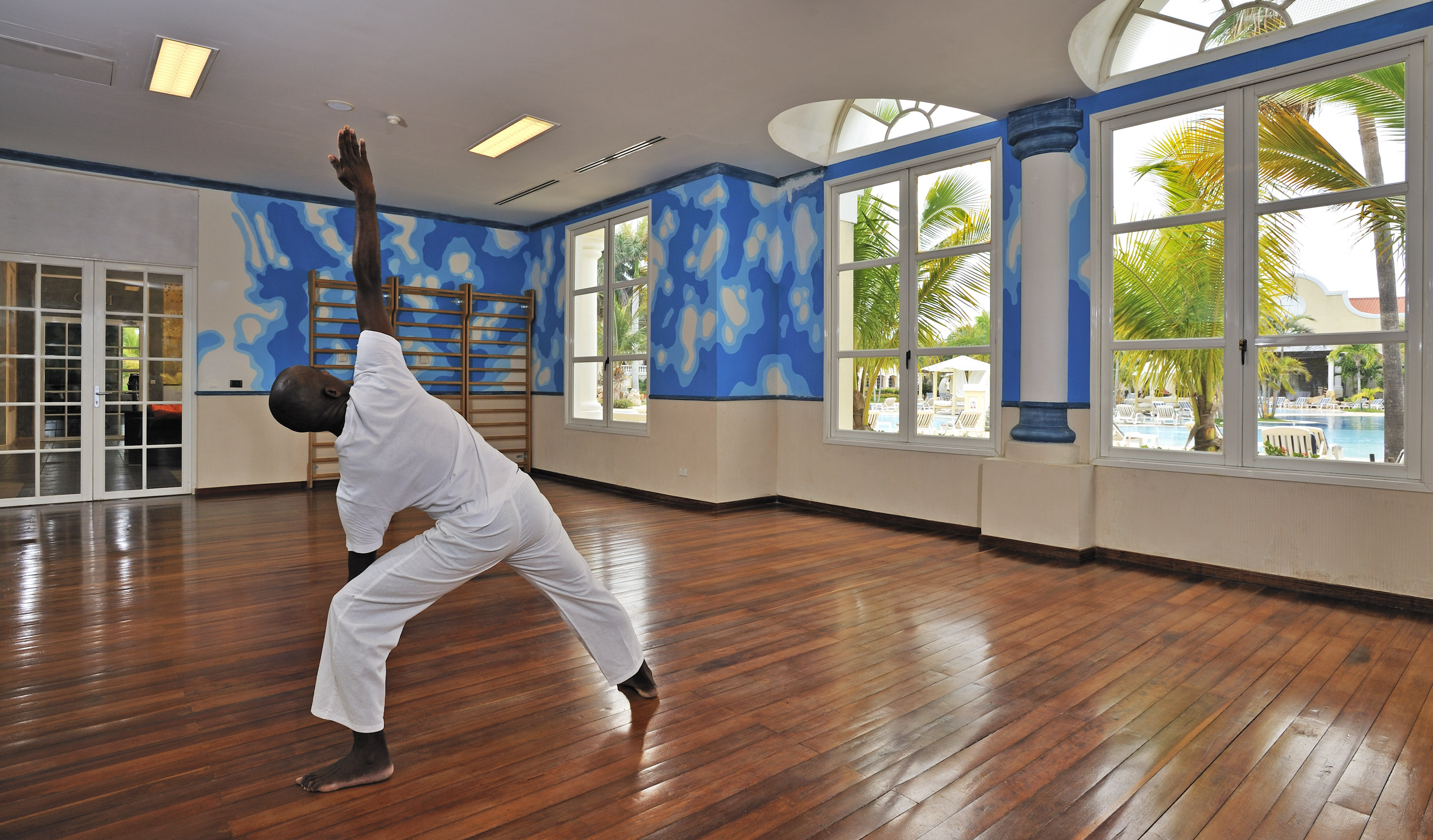 a man in a white uniform doing yoga in a room with blue walls and windows