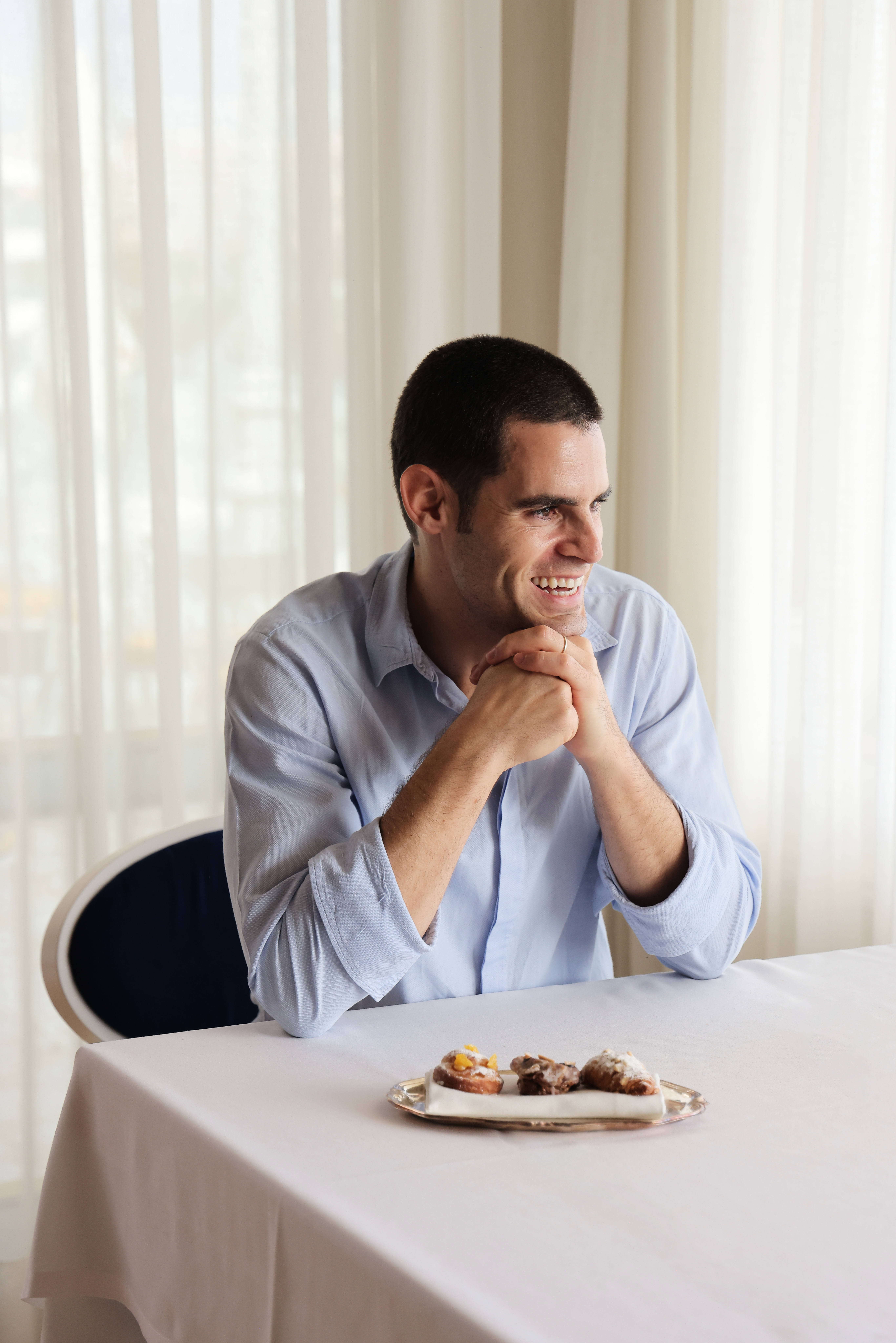 Smiling man in light blue shirt at table with dessert tray.