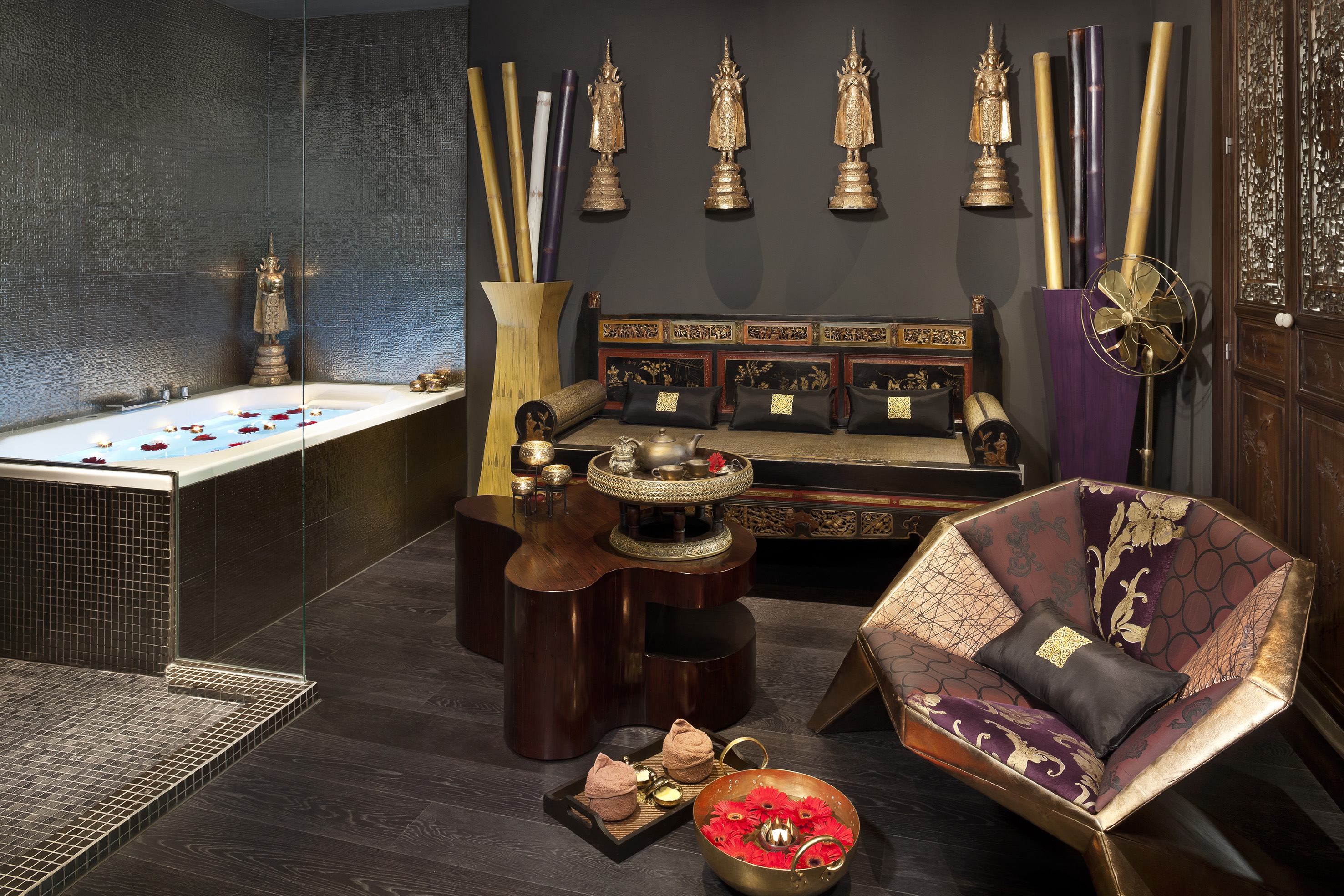 Luxury spa room with petal-filled bathtub, ornate furniture, and Asian decor.