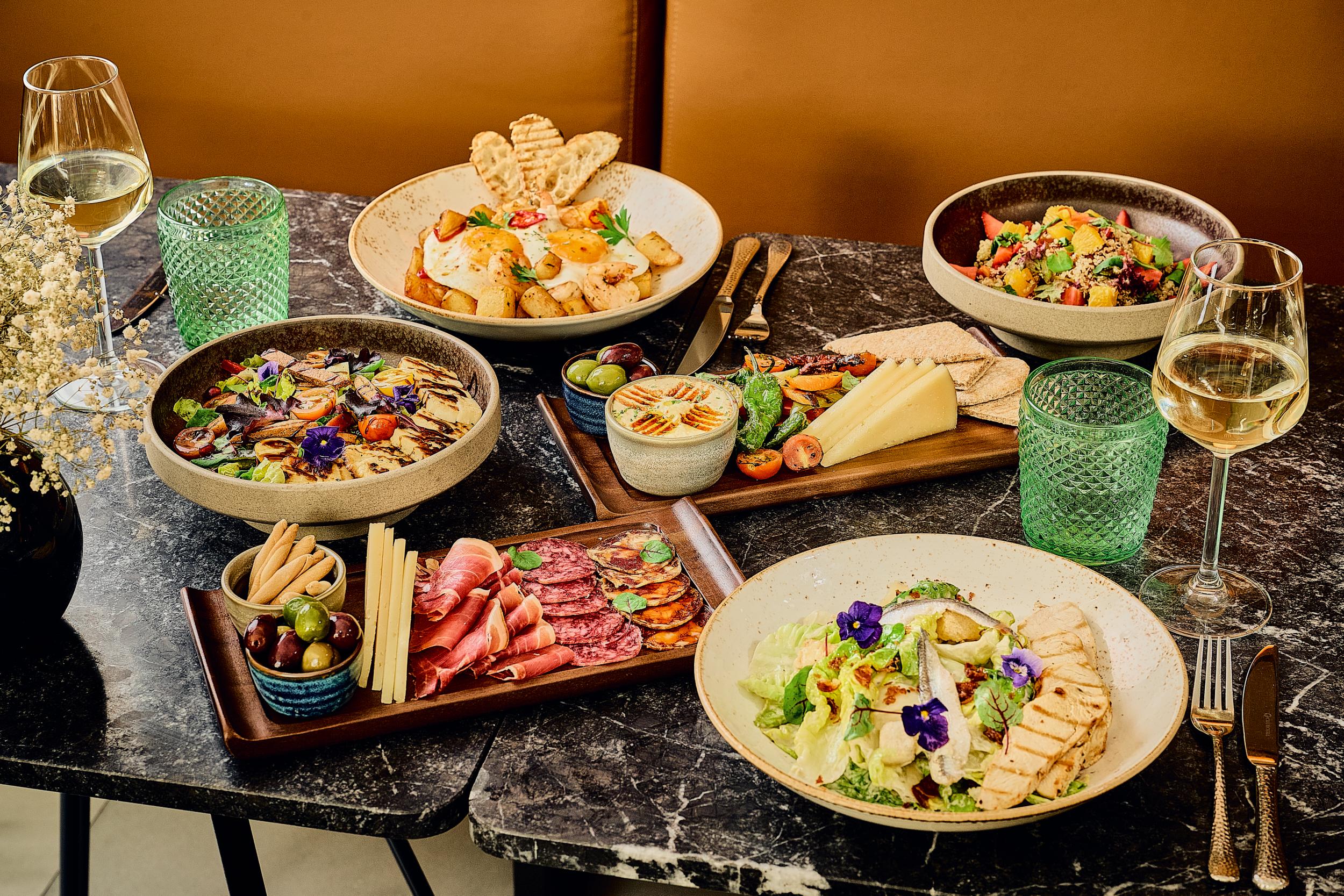 Mediterranean tapas spread: salads, charcuterie, eggs, hummus, cheese, and white wine.