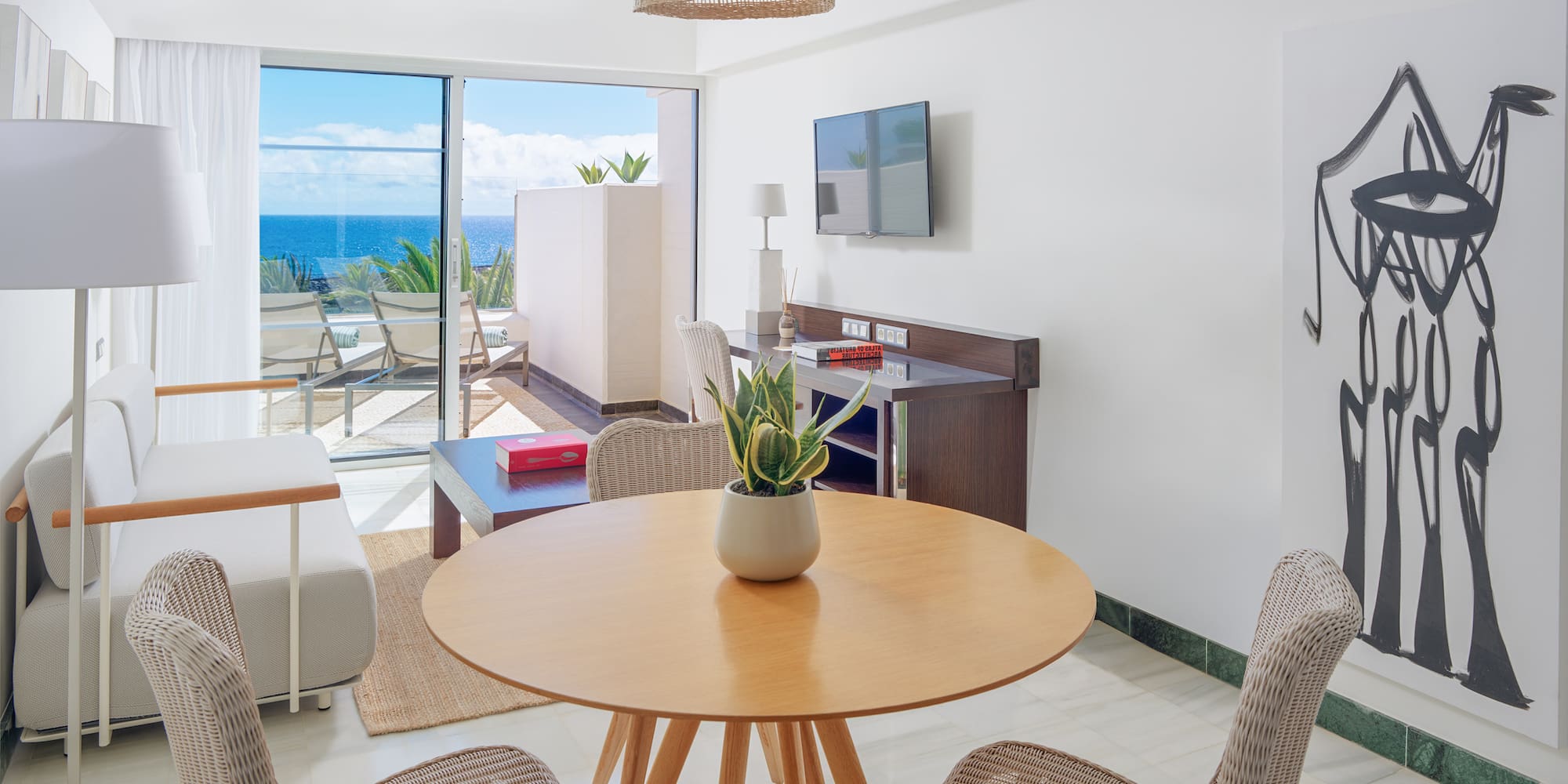 Modern suite living room with ocean view balcony, rattan furniture, and abstract art.