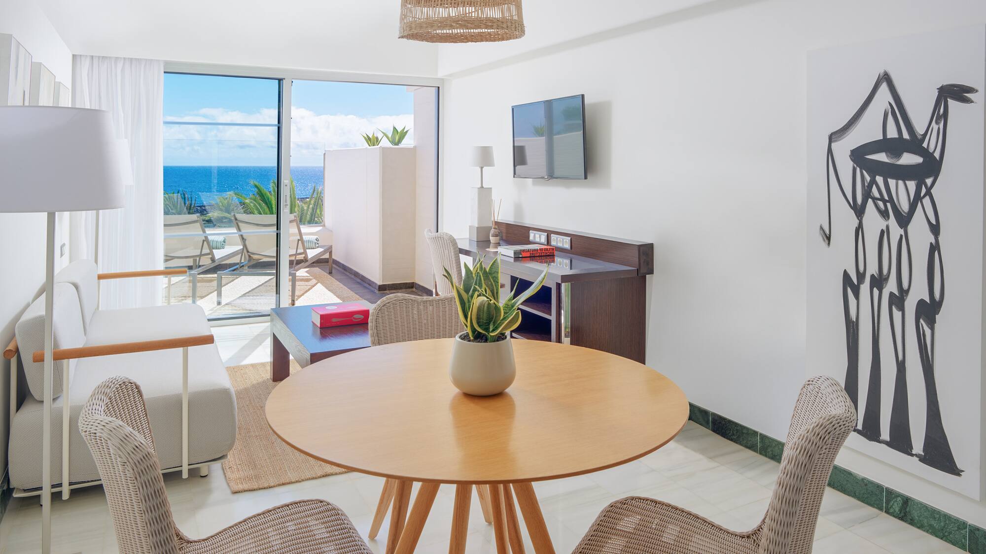 Modern suite living room with ocean view balcony, rattan furniture, and abstract art.